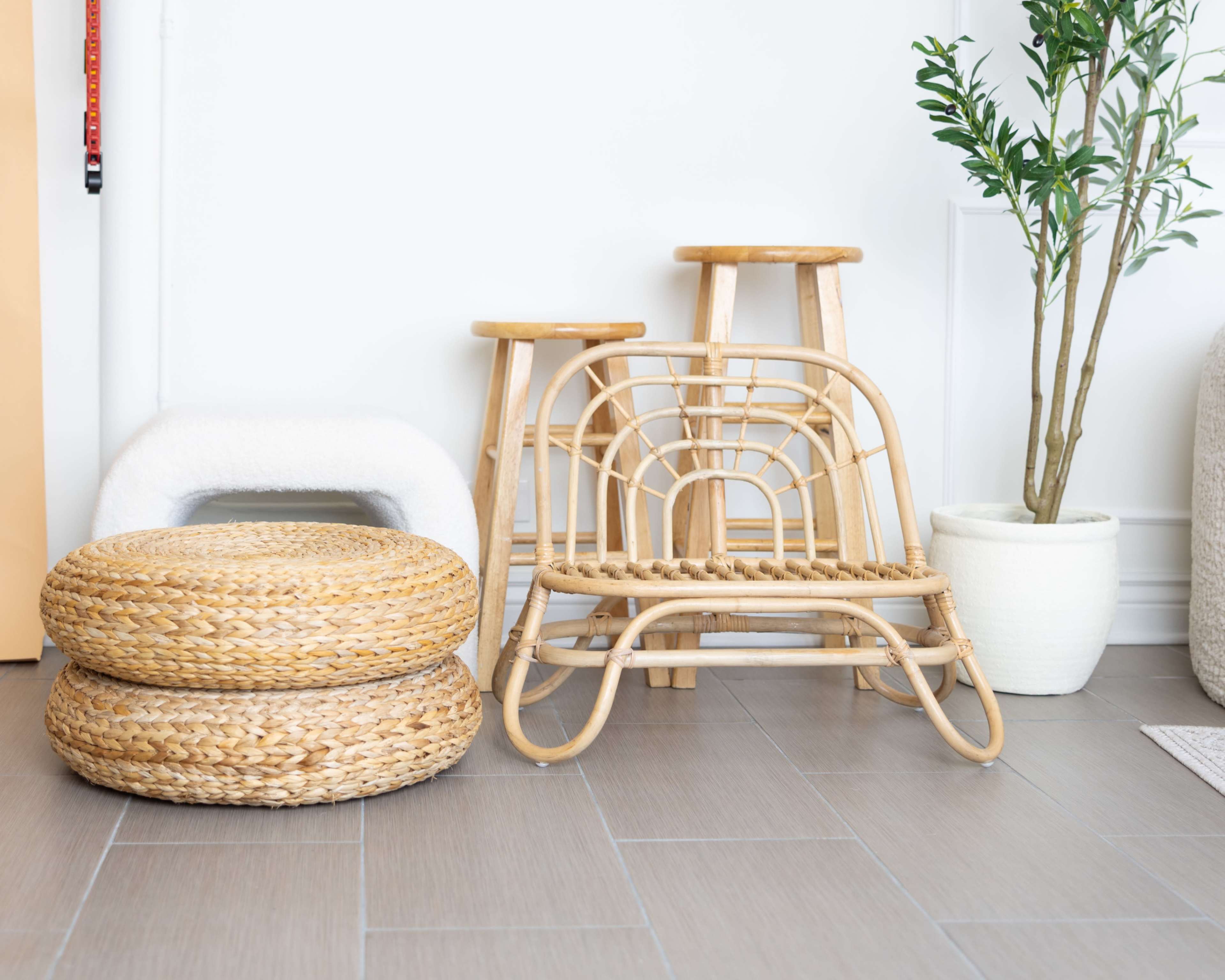 The image features a minimalist living space with a variety of woven seating elements and a potted plant near a white wall.