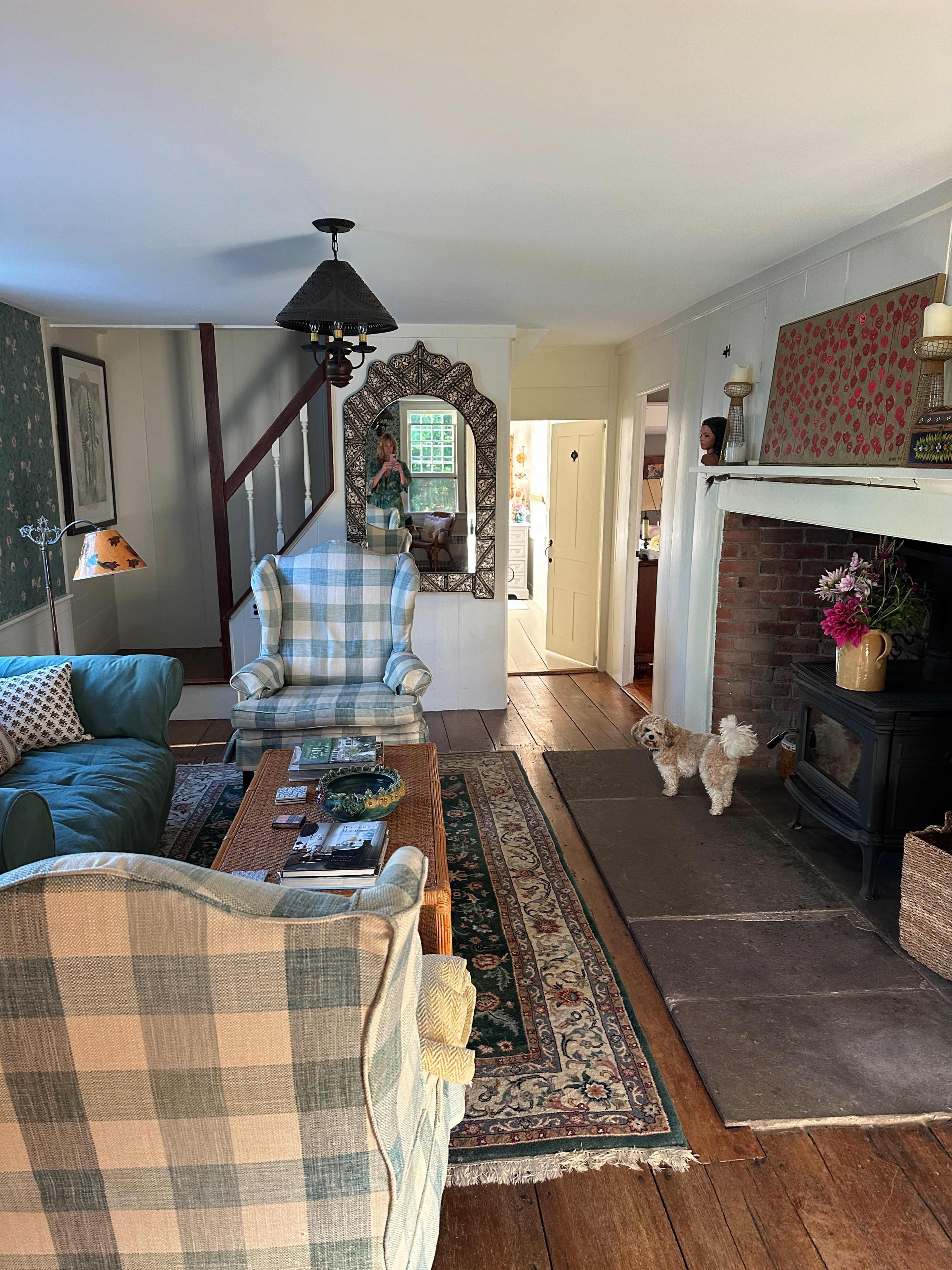 A cozy living room with a sofa, armchairs, a wooden coffee table, and a dog standing on a stone floor near a fireplace.