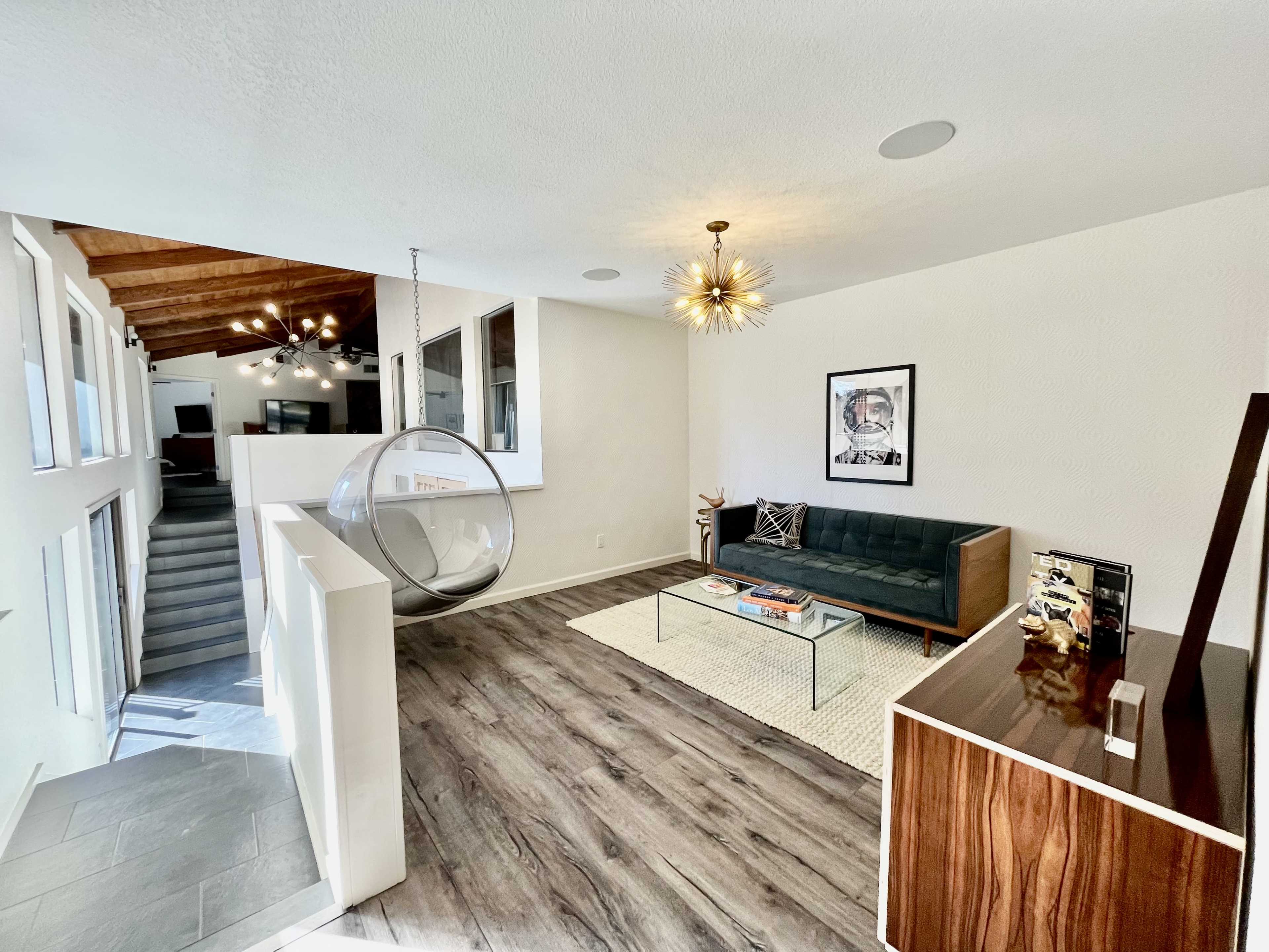 A modern living room featuring a sleek sofa, a glass coffee table, and a hanging chair, with large windows allowing ample natural light.