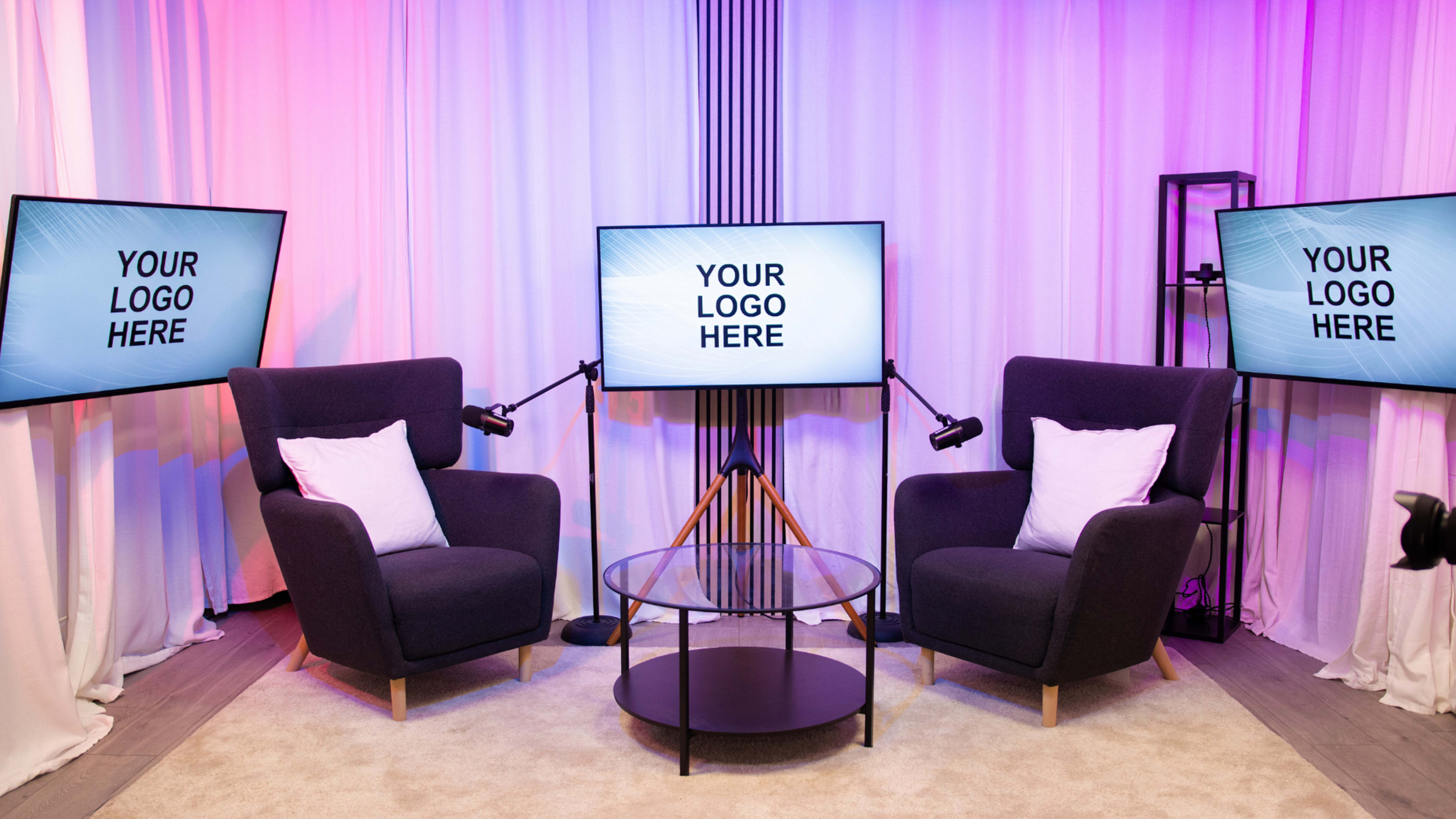A modern interview setup features two chairs, a circular glass table, and three screens displaying the text "YOUR LOGO HERE."