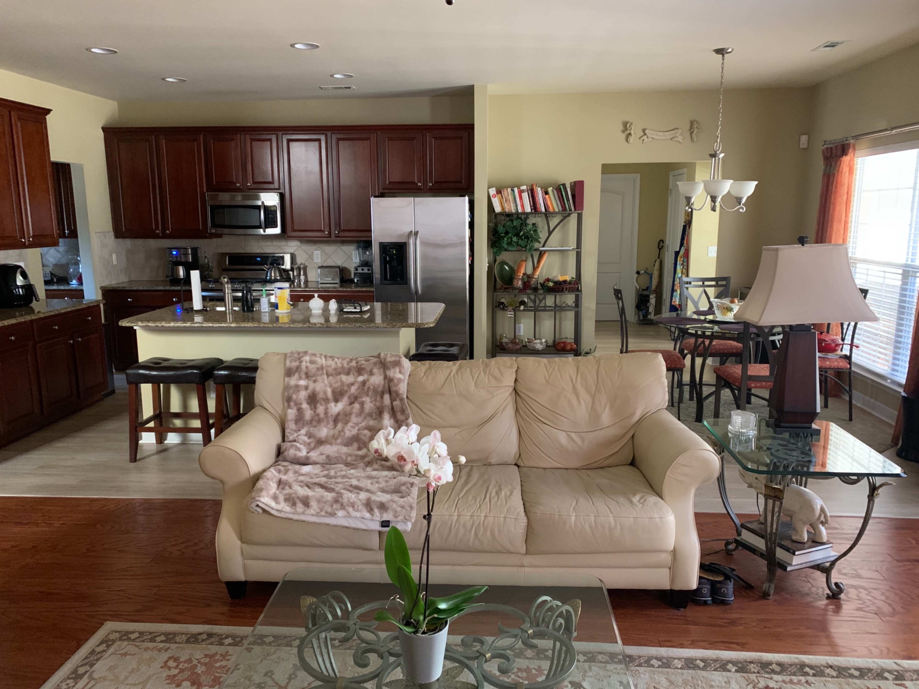 A cozy living space featuring a beige sofa with a throw blanket, a glass coffee table, and an open kitchen area with dark wood cabinetry and stainless steel appliances.