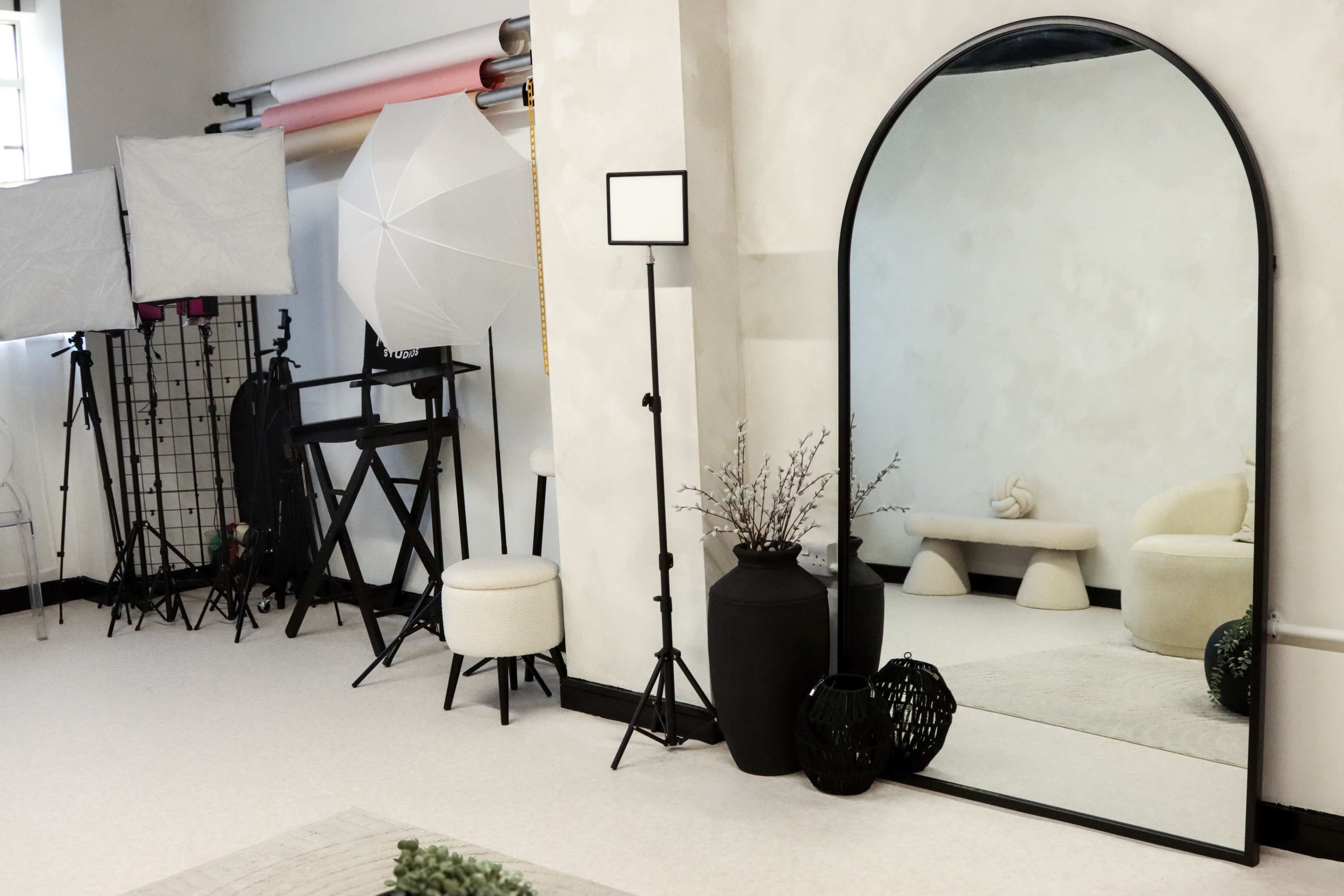 The image features a neatly arranged photography studio with soft lighting equipment, a large mirror, and various decorative elements on display.