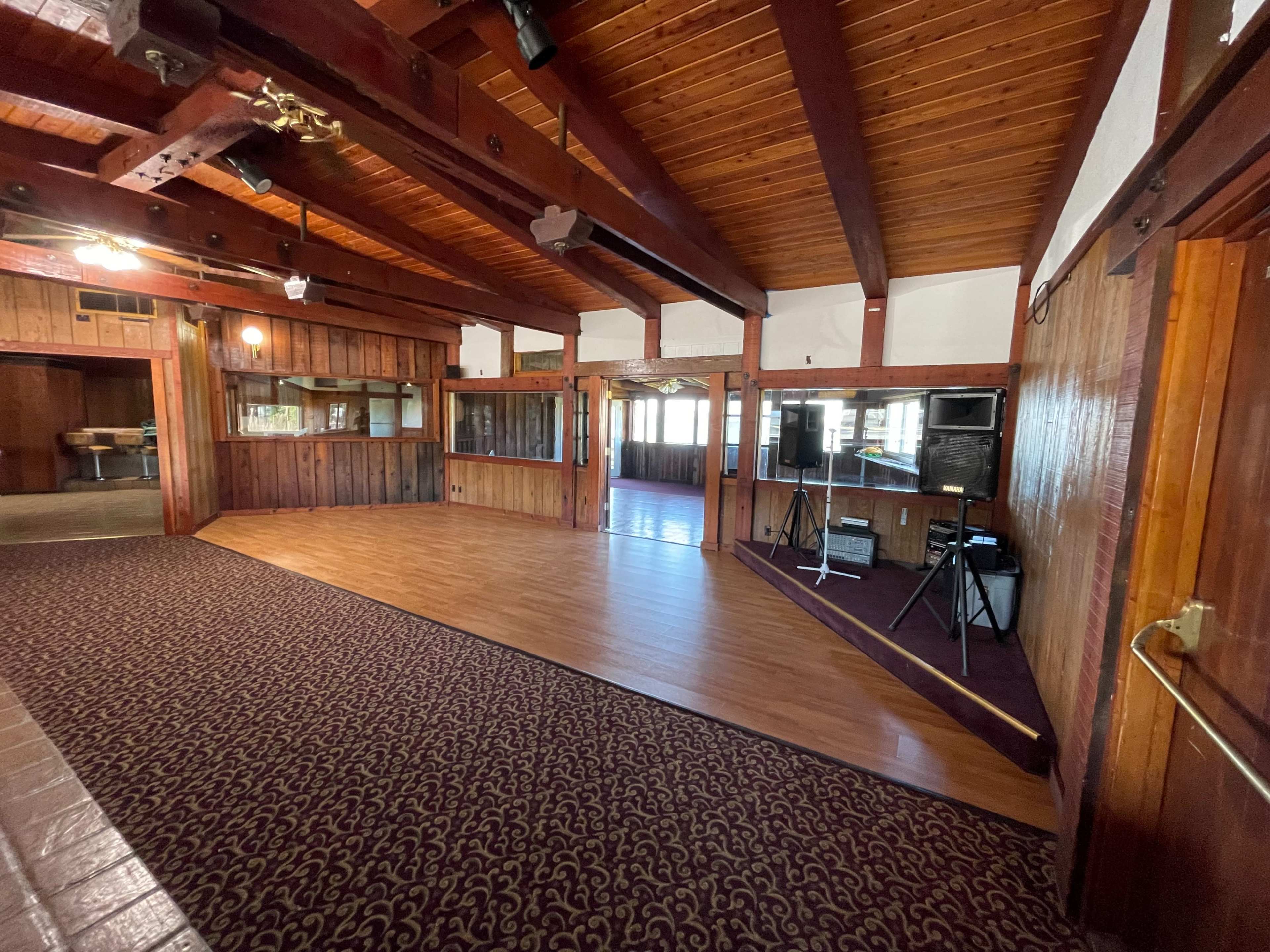 The interior of a wooden banquet hall features a raised wooden floor area with large windows and a patterned carpet.
