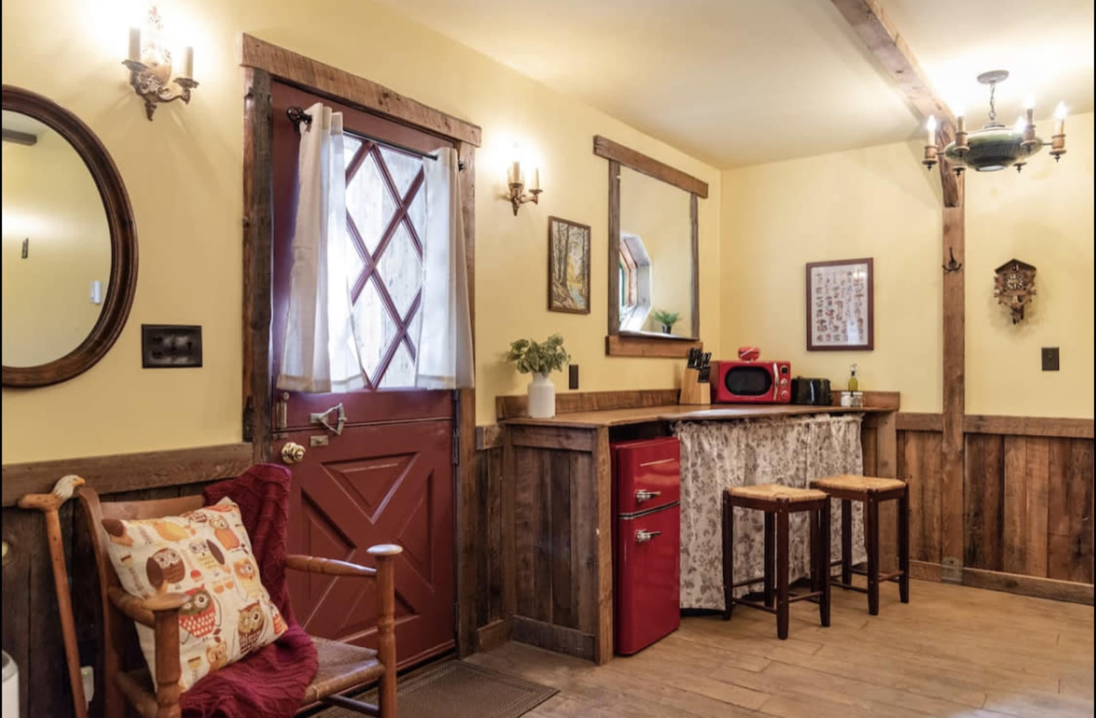 The scene depicts a rustic kitchen area with a red refrigerator, a wooden bar counter with stools, and a warm yellow wall.