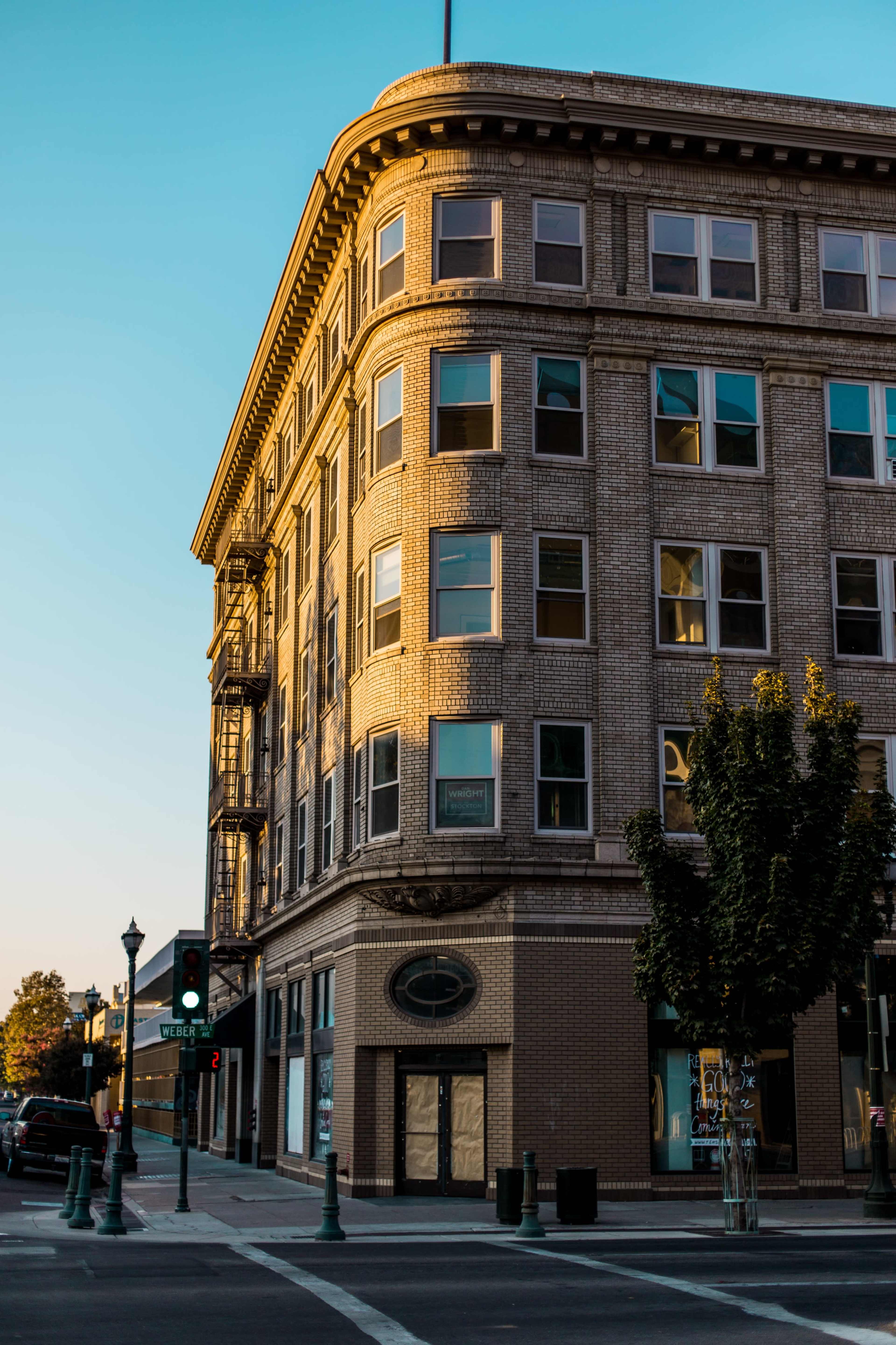 A historic brick building with large windows and decorative trim stands at an intersection in the late afternoon light.