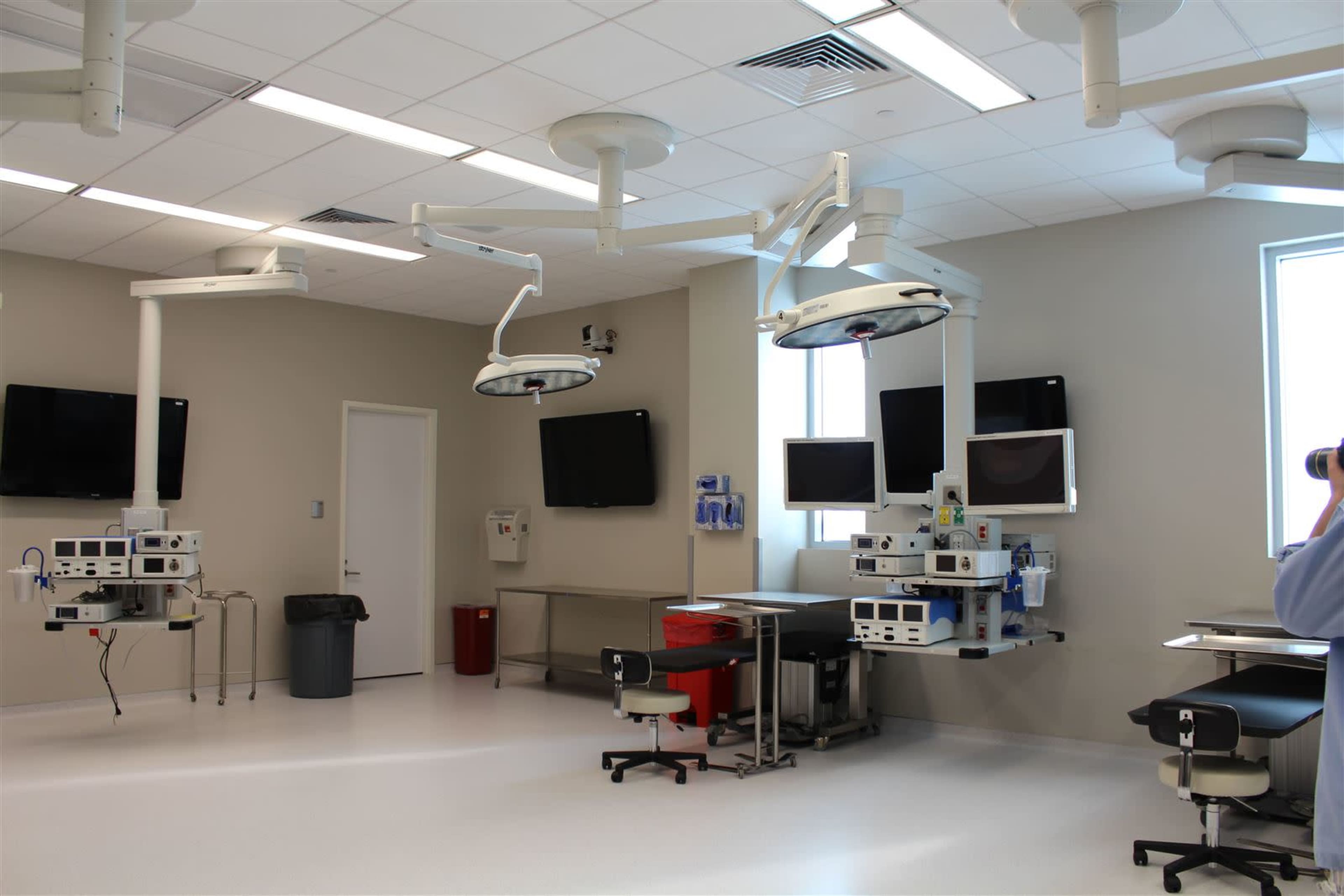 A modern operating room with surgical lights, monitors, and medical equipment organized along the walls.