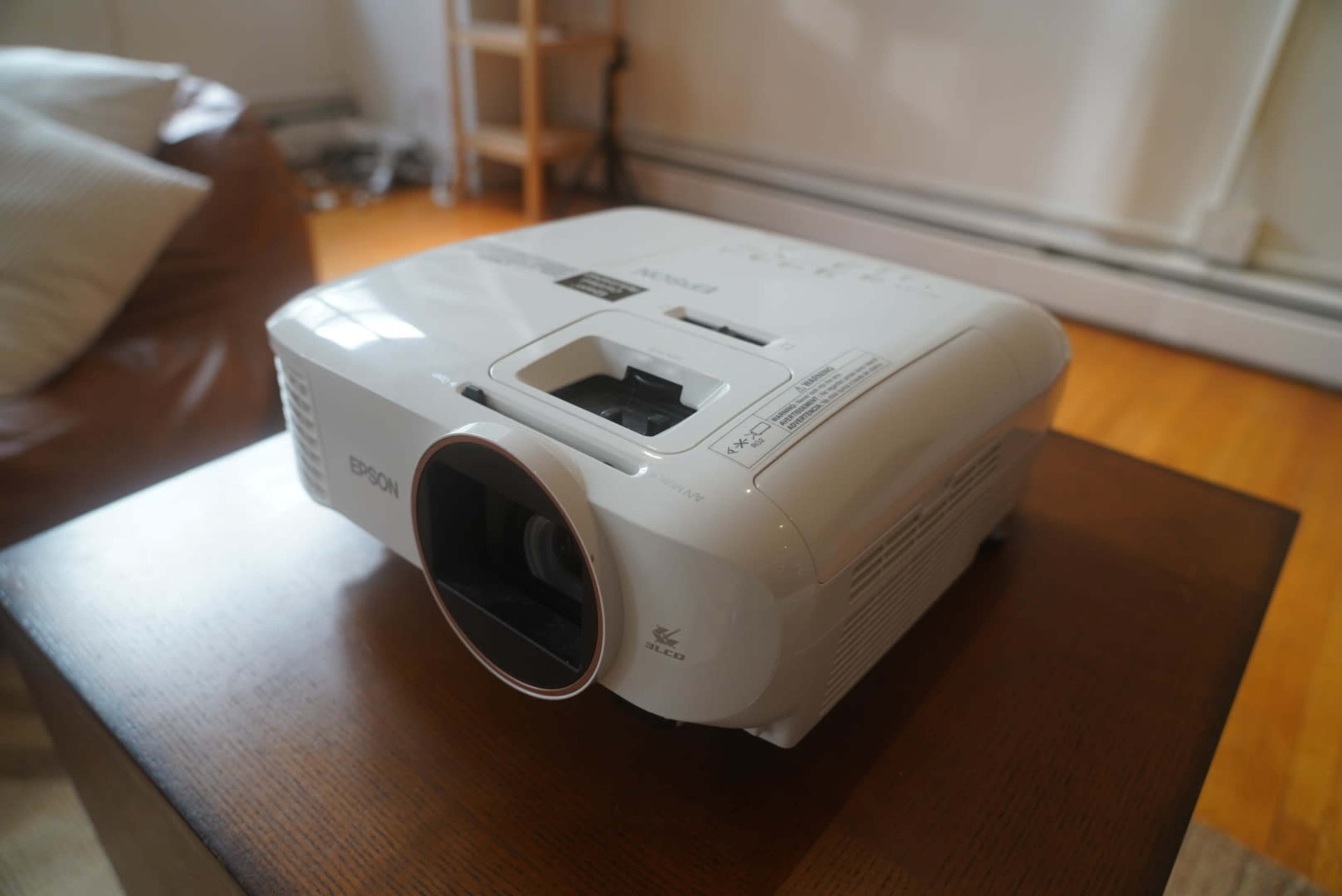 A white Epson projector is positioned on a wooden table in a well-lit room.