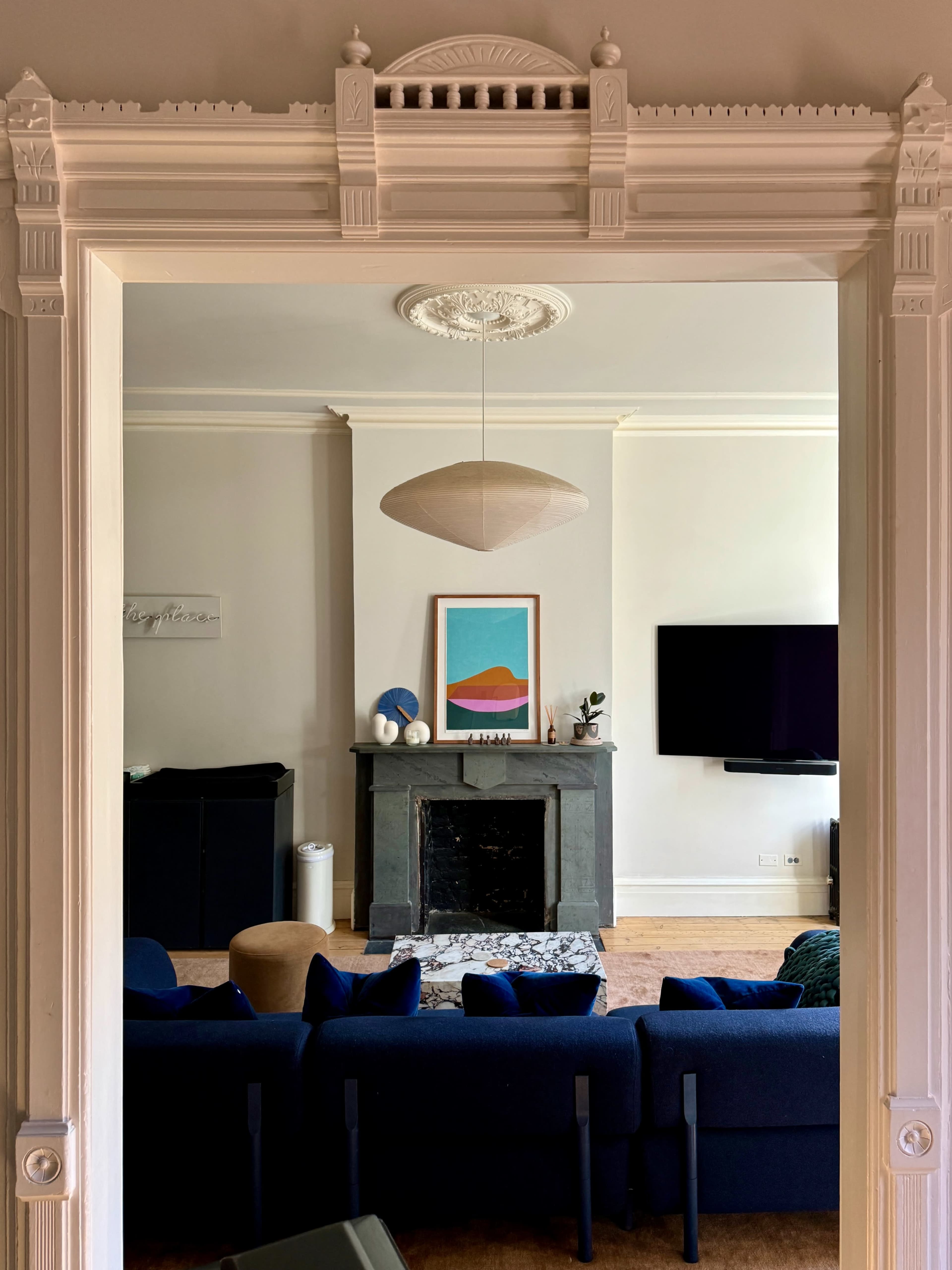 A view through an ornate doorway reveals a living room featuring a dark fireplace, a wall-mounted TV, and a blue sofa facing a colorful piece of art.