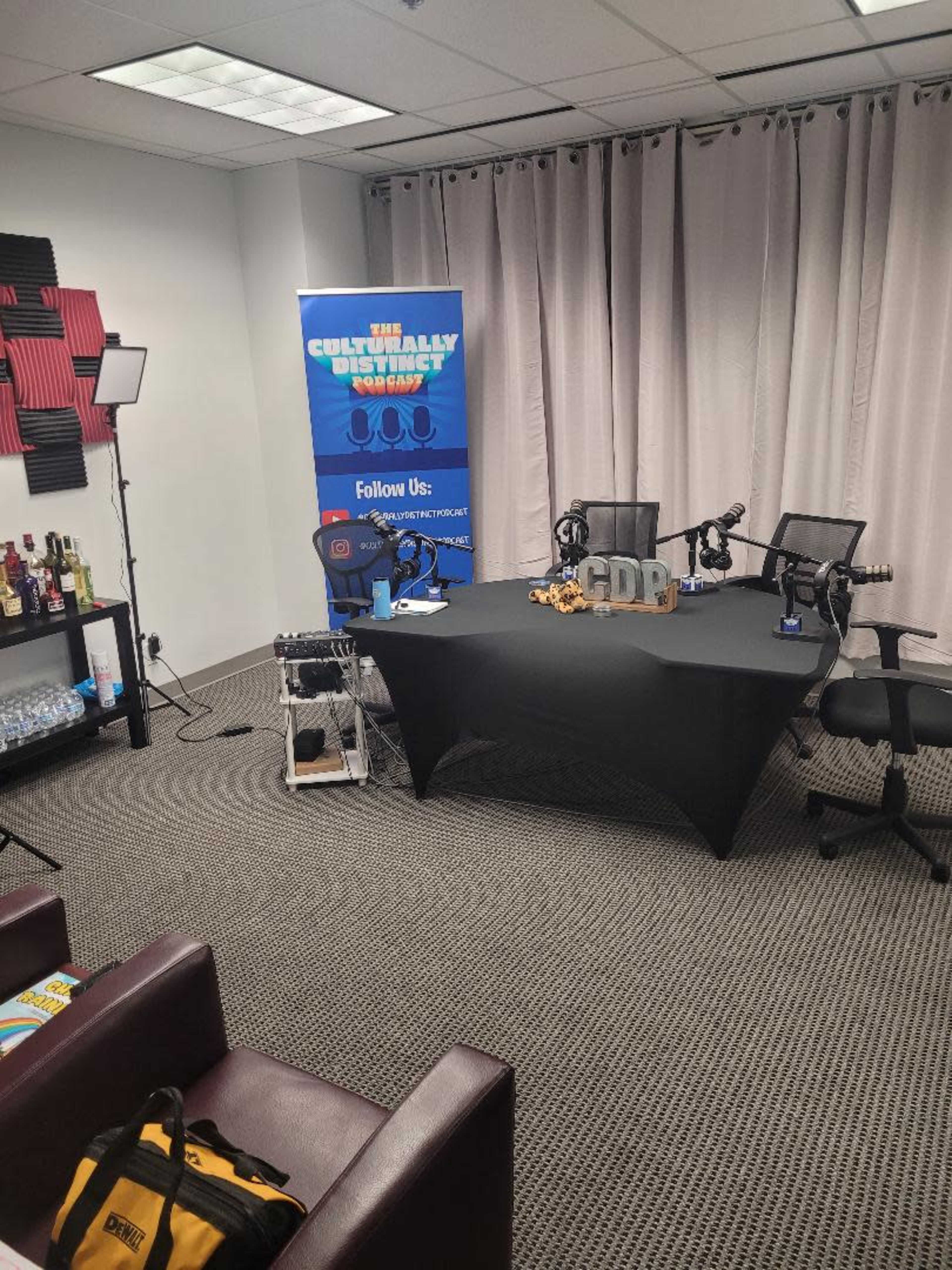 The image shows a podcast studio setup with a table, microphones, chairs, and a backdrop featuring the title "The Culturally Distinct Show."