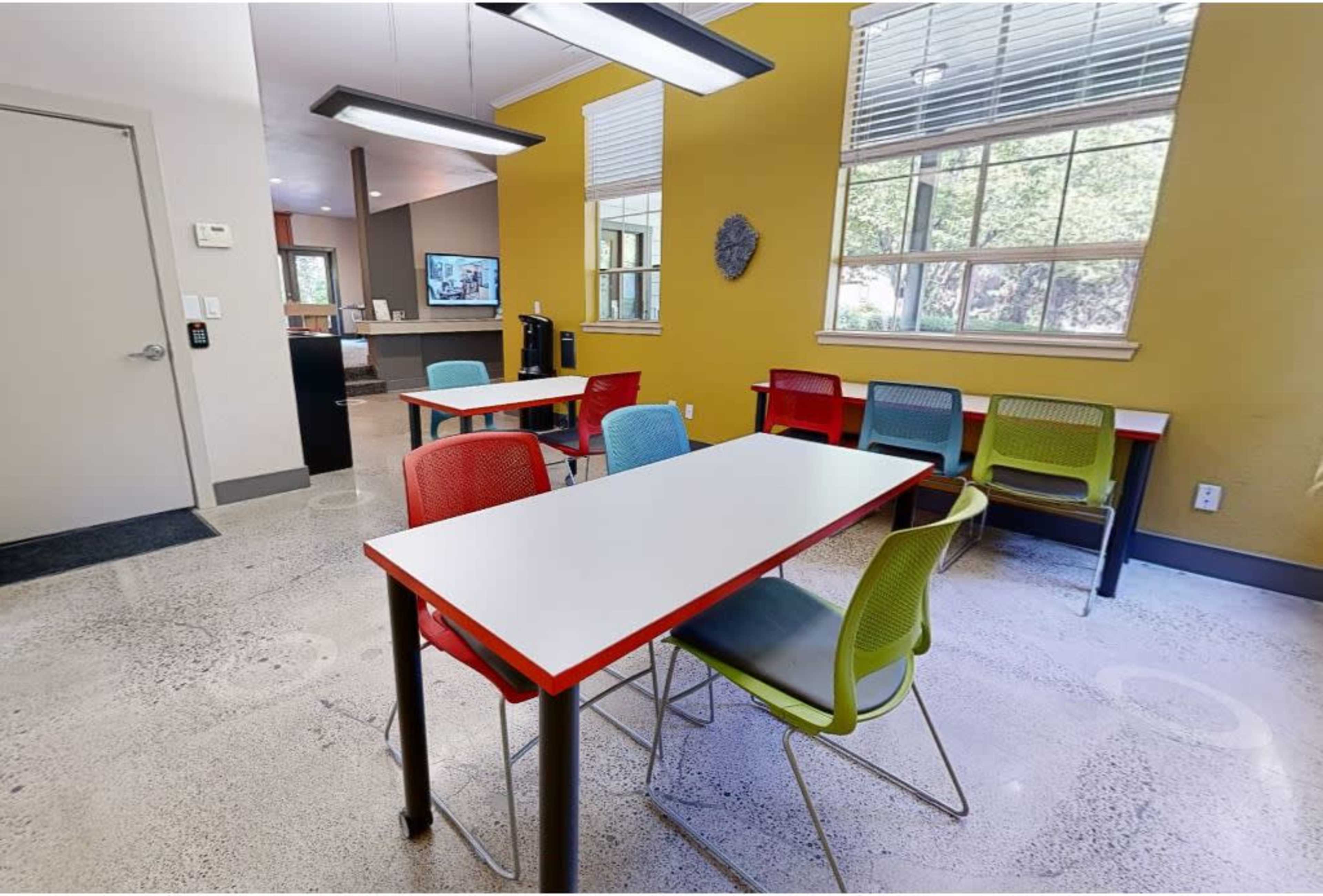 A brightly lit room with several tables and colorful chairs arranged around a polished concrete floor.