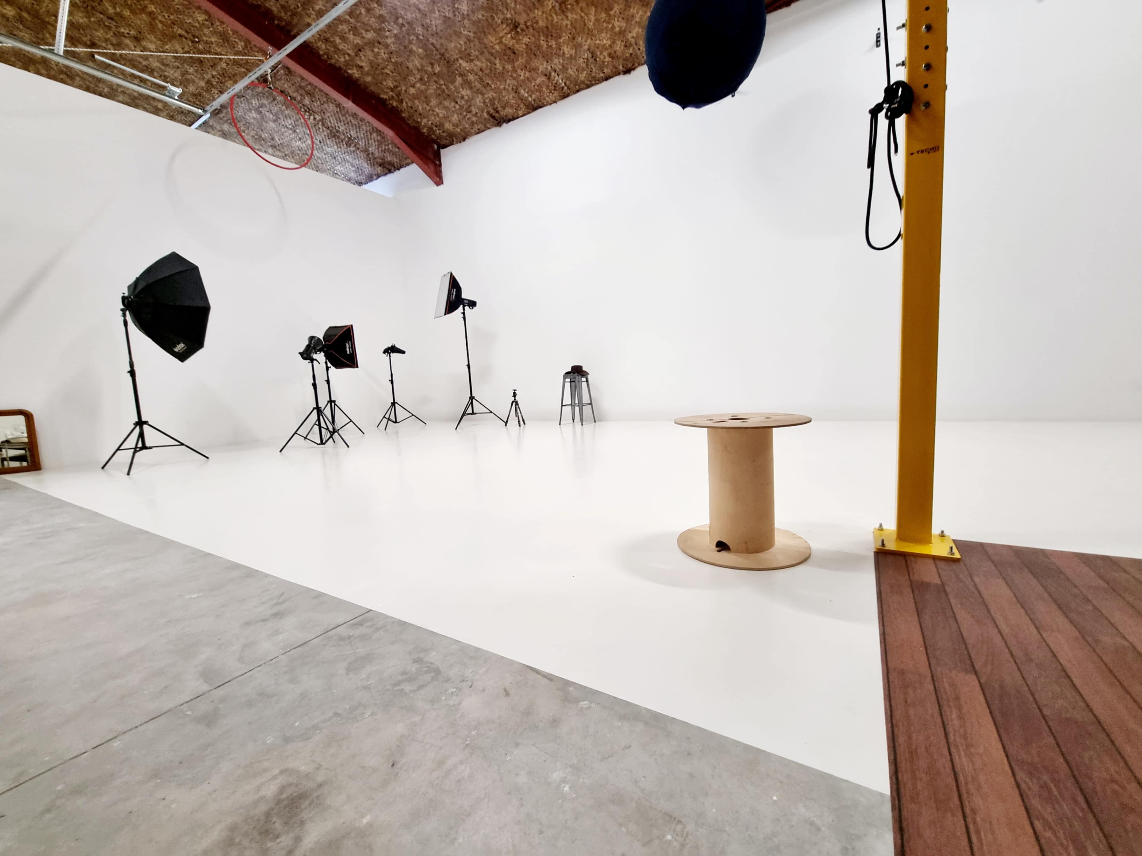 A photography studio with several light stands, backdrops, and a wooden spool on a polished white floor.