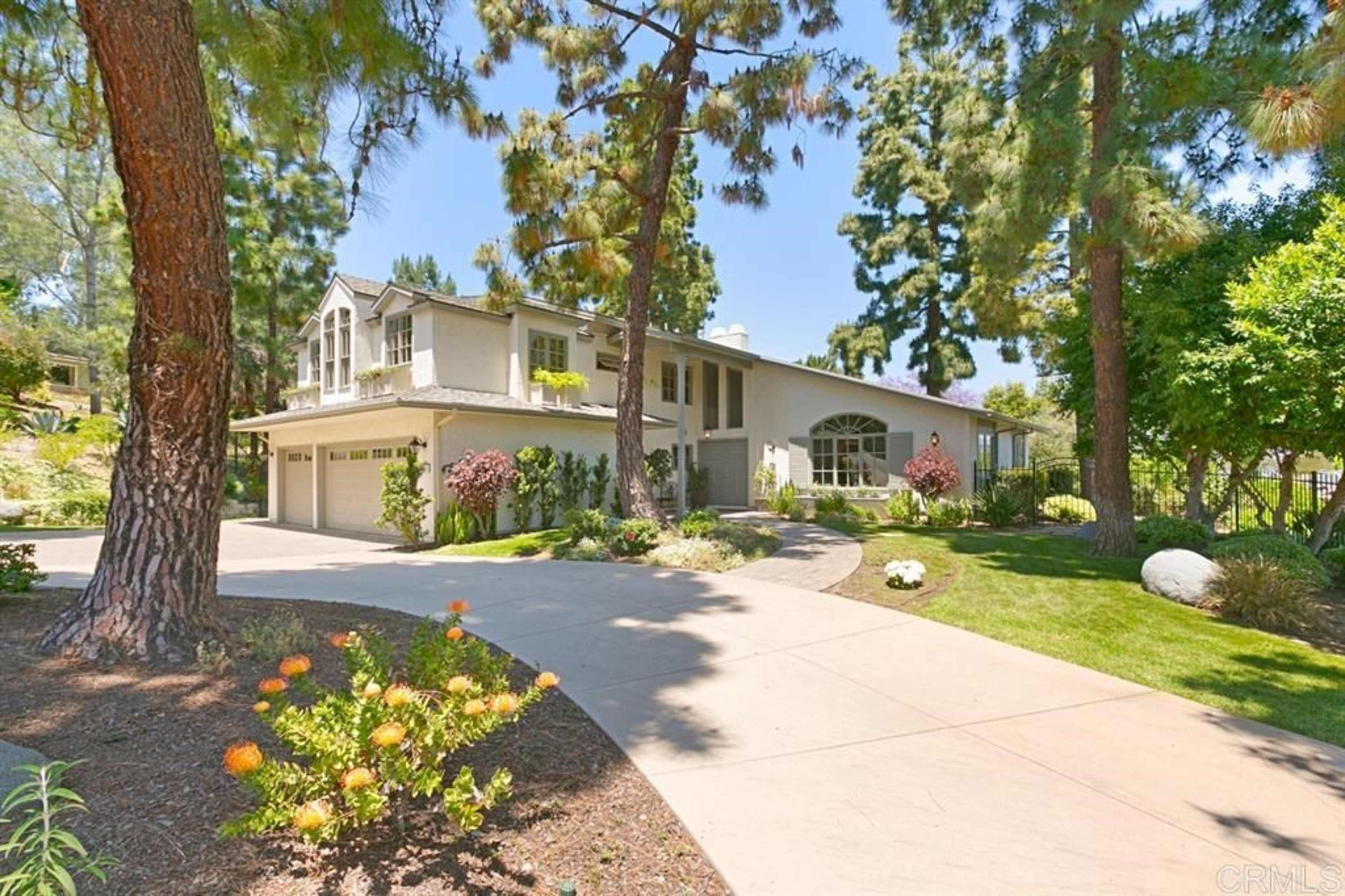 A two-story house with a landscaped front yard and a curved driveway lined with trees.