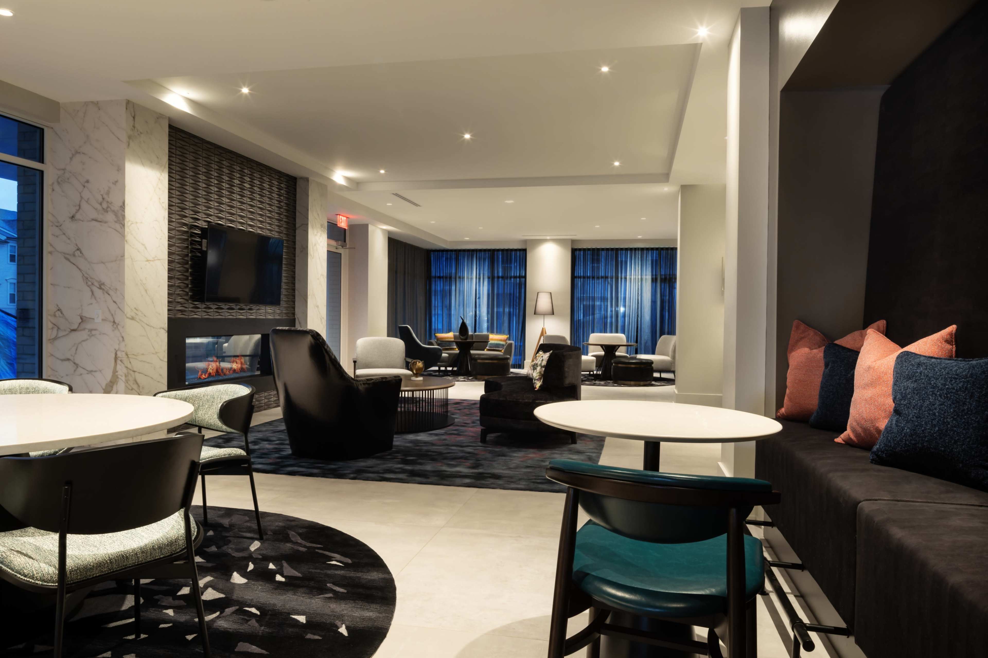 A modern lounge area with comfortable seating, a fireplace, and large windows allowing natural light to enter the space.