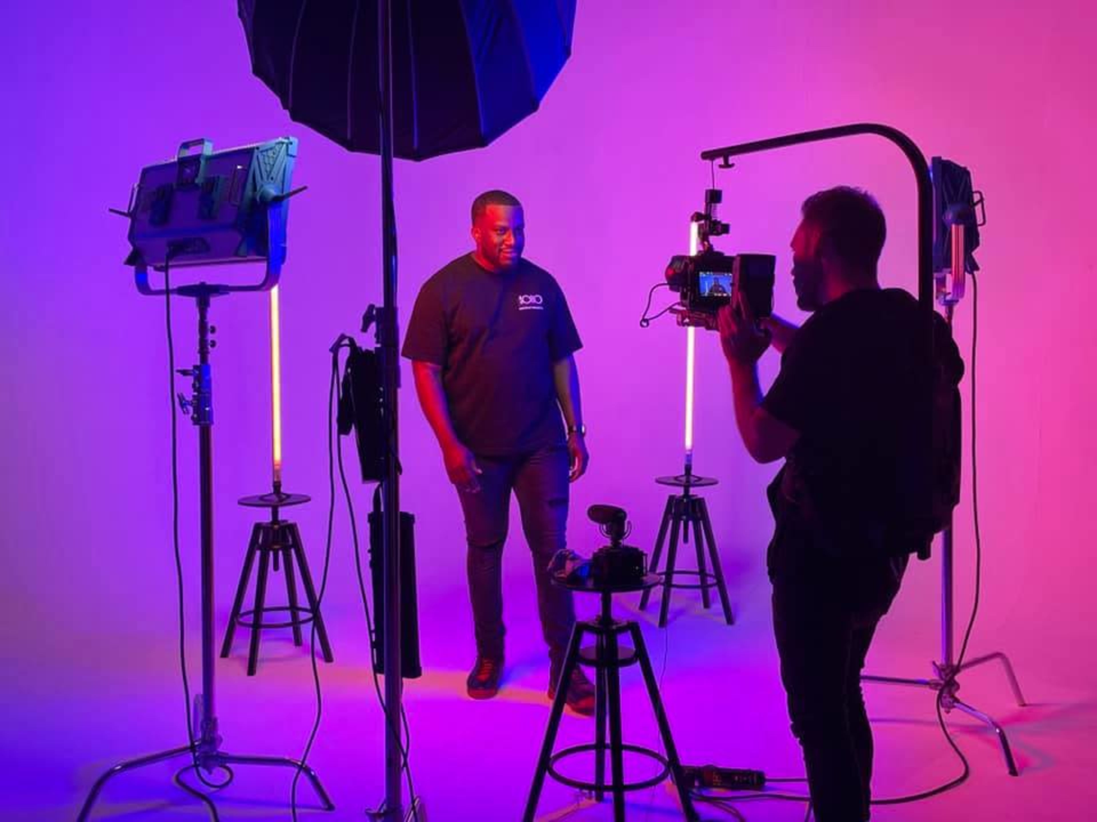 A man poses under studio lighting while a photographer captures images with a camera on a tripod.