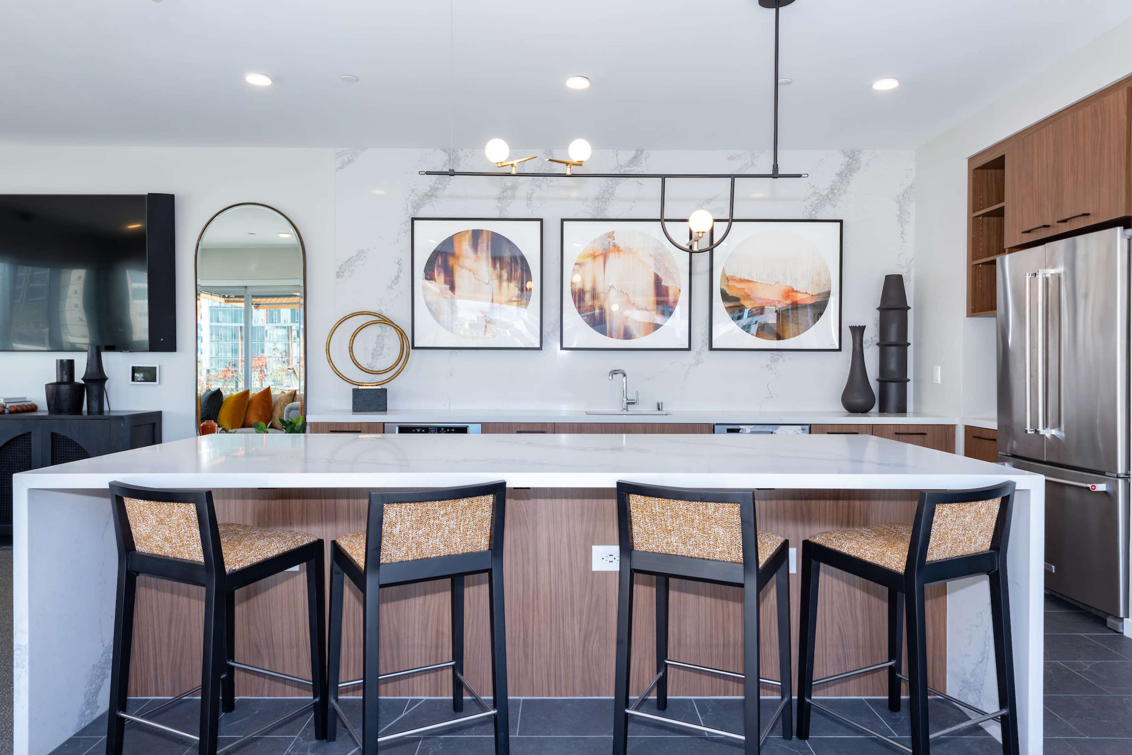 A modern kitchen features a large island with bar seating, framed artwork on the walls, and sleek stainless steel appliances.