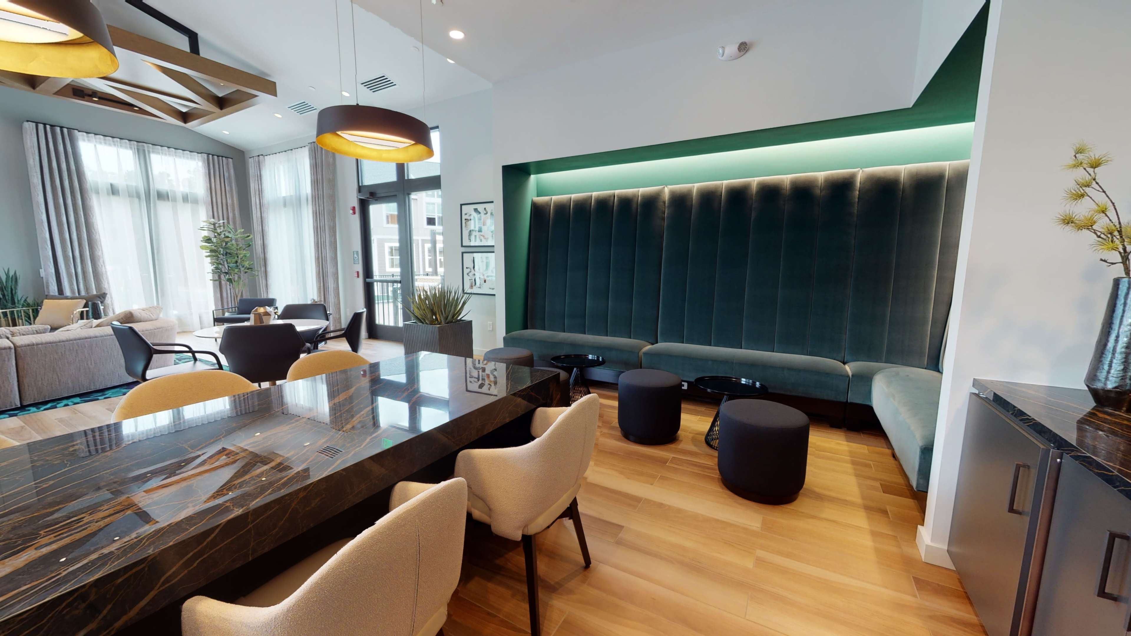 A modern lounge area with a dark marble table, upholstered seating, and large windows providing natural light.