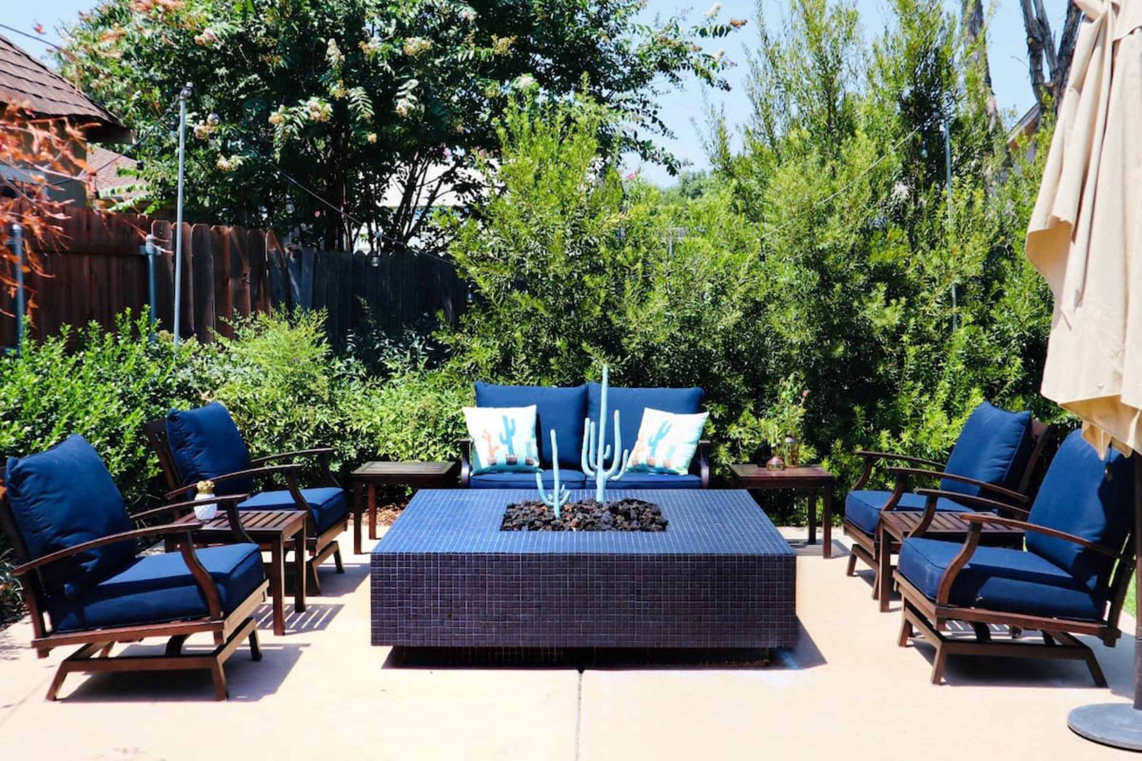A patio seating area with four blue cushioned chairs surrounding a rectangular table featuring a decorative plant centerpiece.