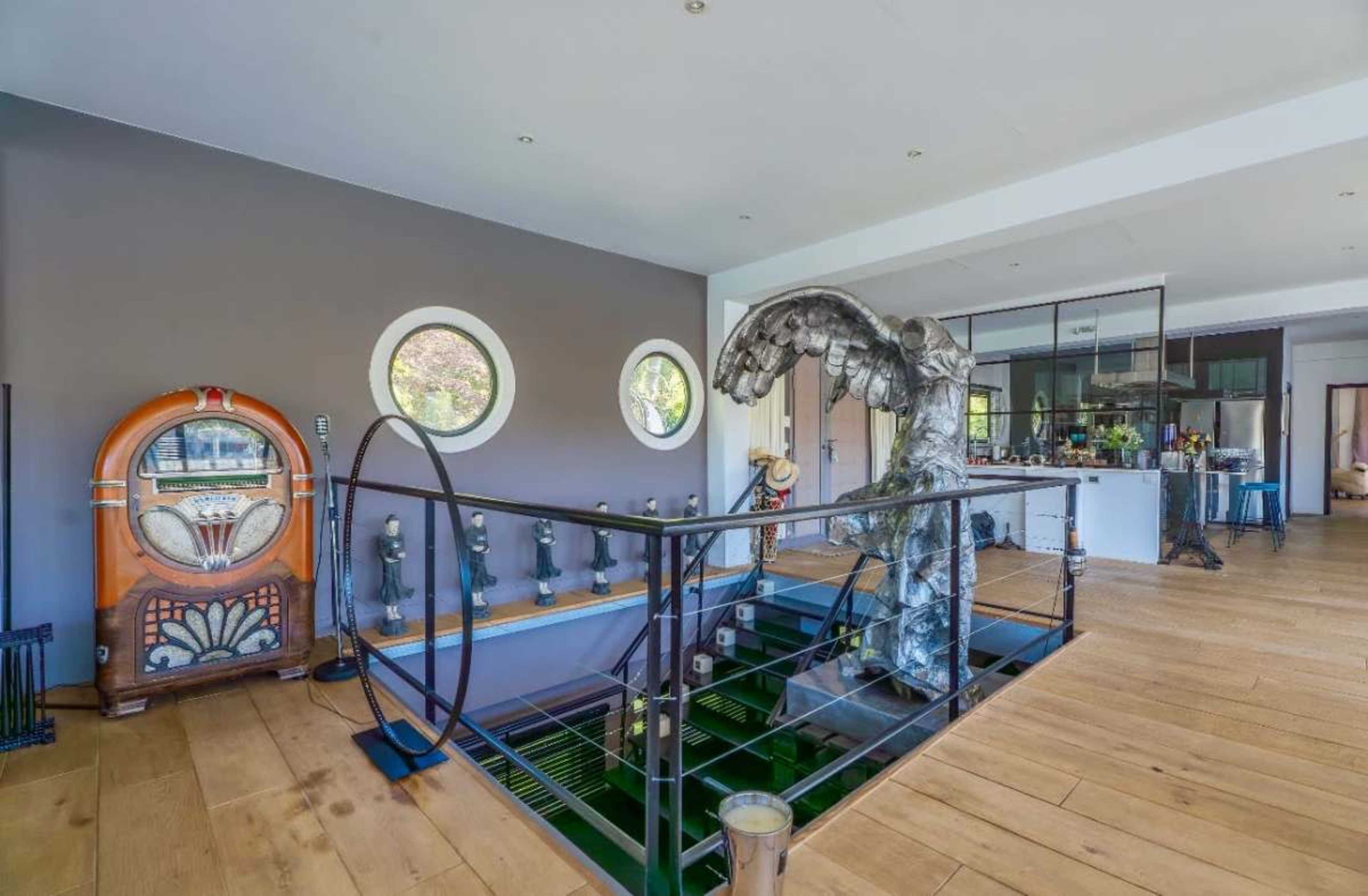 The image shows a modern interior with a staircase featuring a large artistic installation, a vintage jukebox, and circular windows.