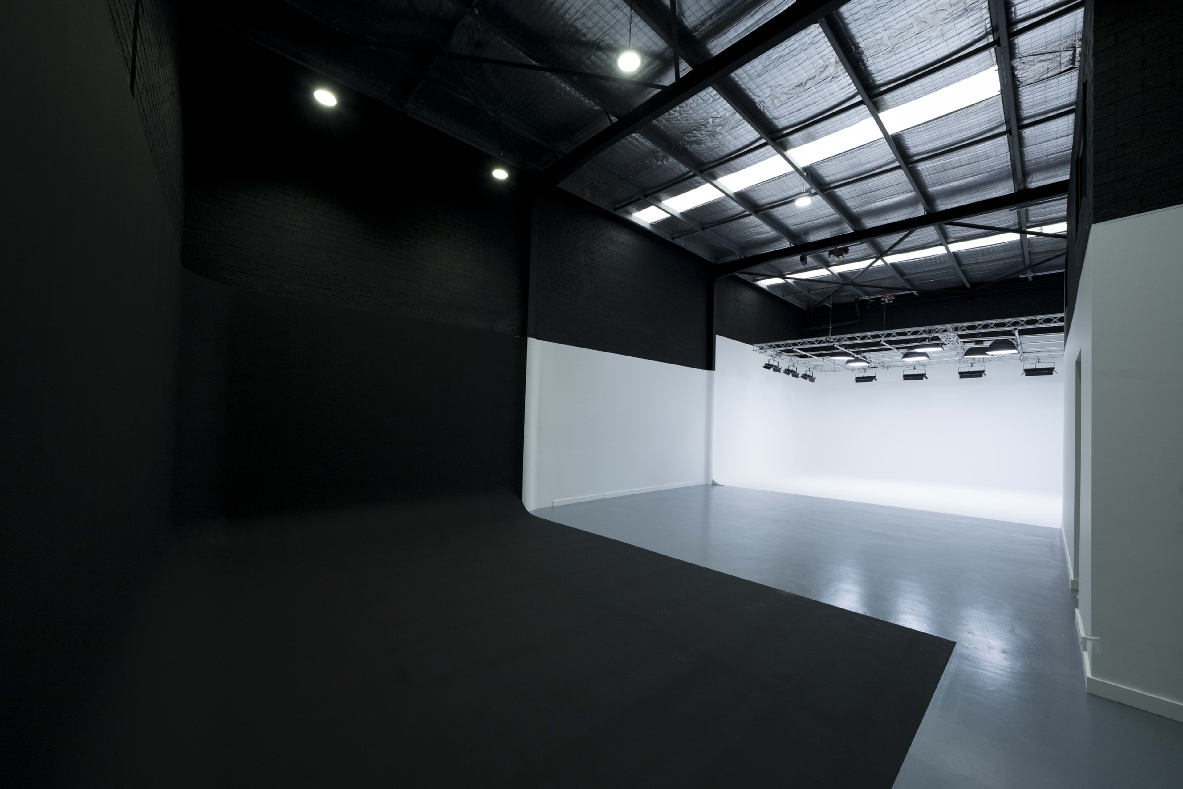 The image shows a spacious photography studio with a large, white backdrop and a dark, textured wall on one side.