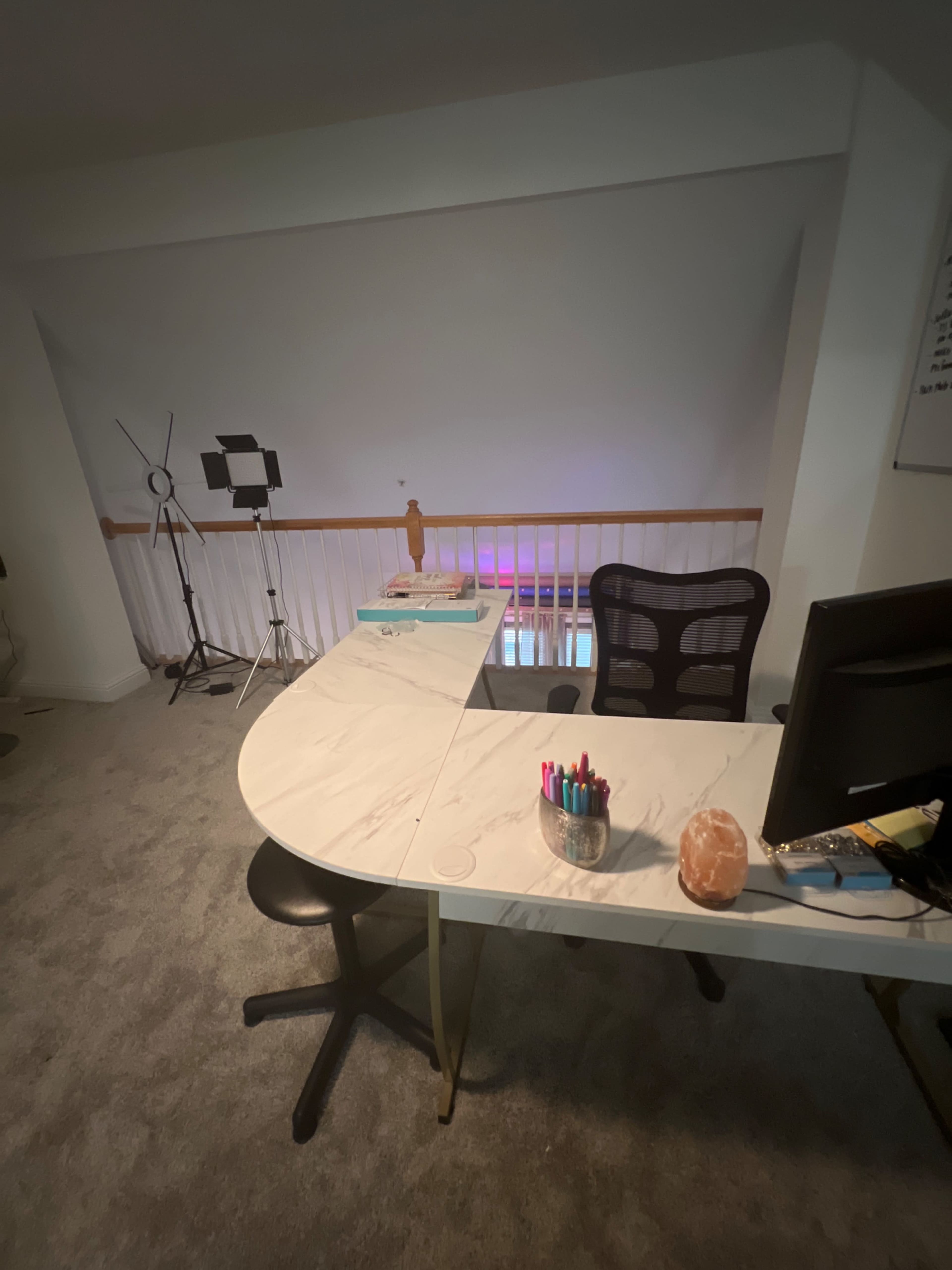 The image shows a simple office setup featuring a marble desk with stationary, a black chair, and a computer monitor, with a background of soft lighting and a tripod.