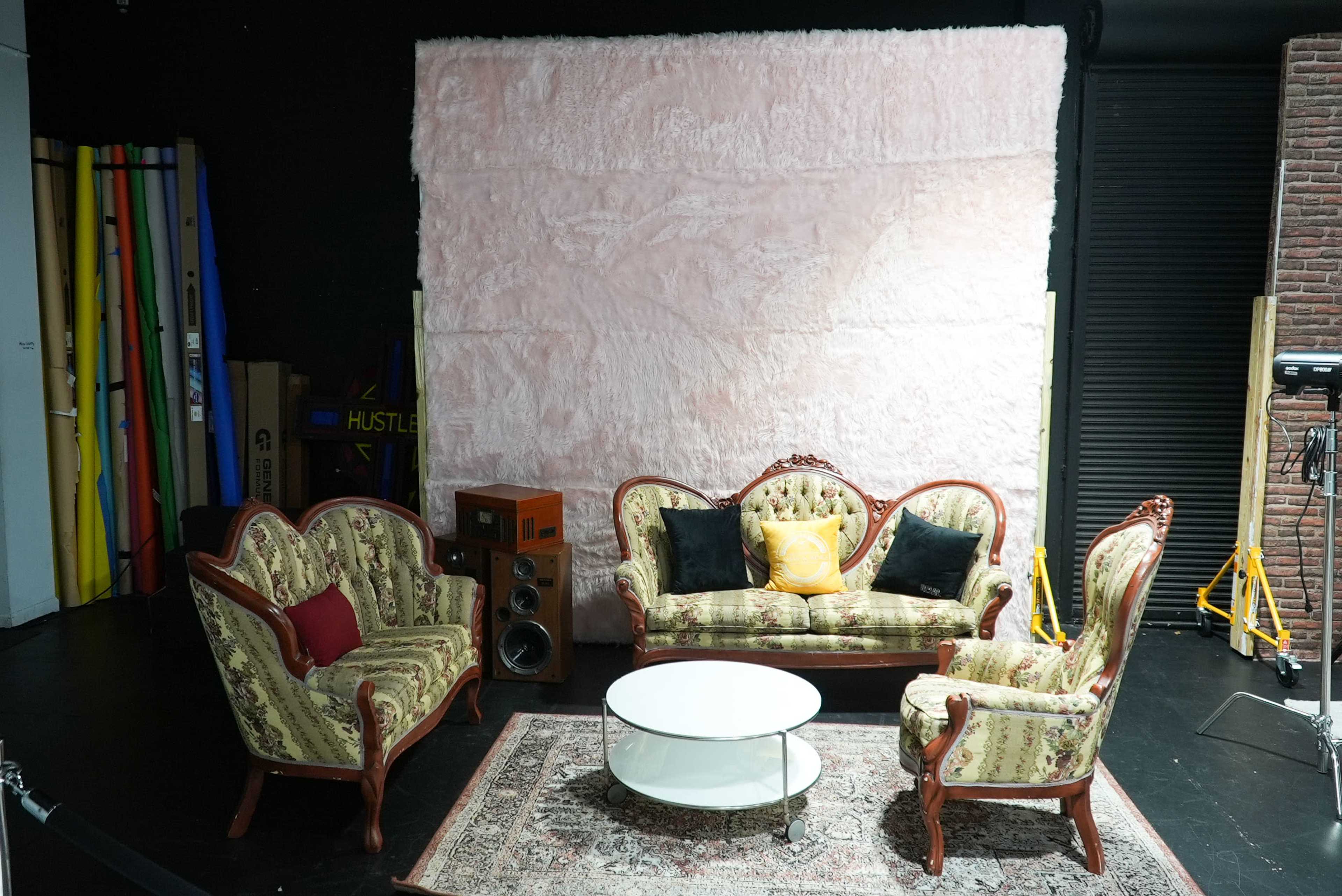 A cozy seating area with vintage floral-patterned couches, a white coffee table, and a textured pink backdrop.