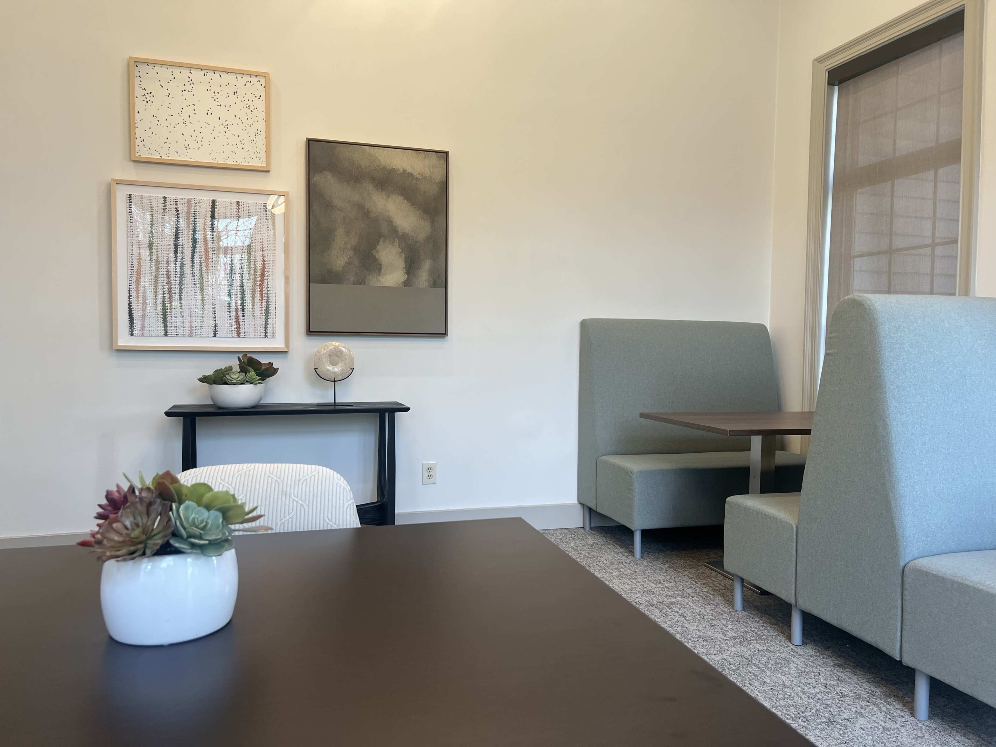 A modern interior with two upholstered booths facing a table, framed wall art, and a small decorative arrangement on a nearby surface.