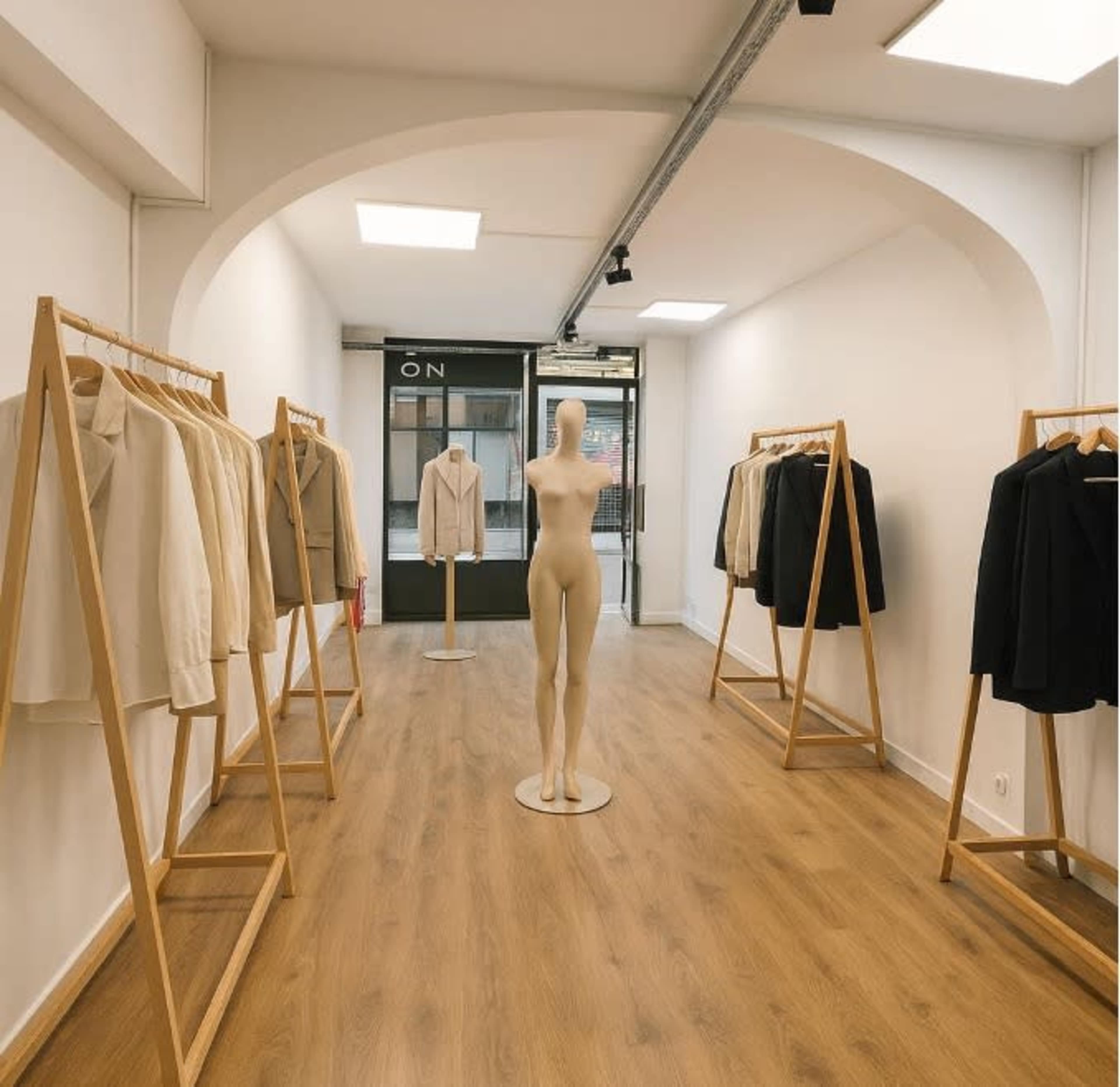 A clothing store interior features a central mannequin and wooden racks displaying various jackets and blazers on either side.