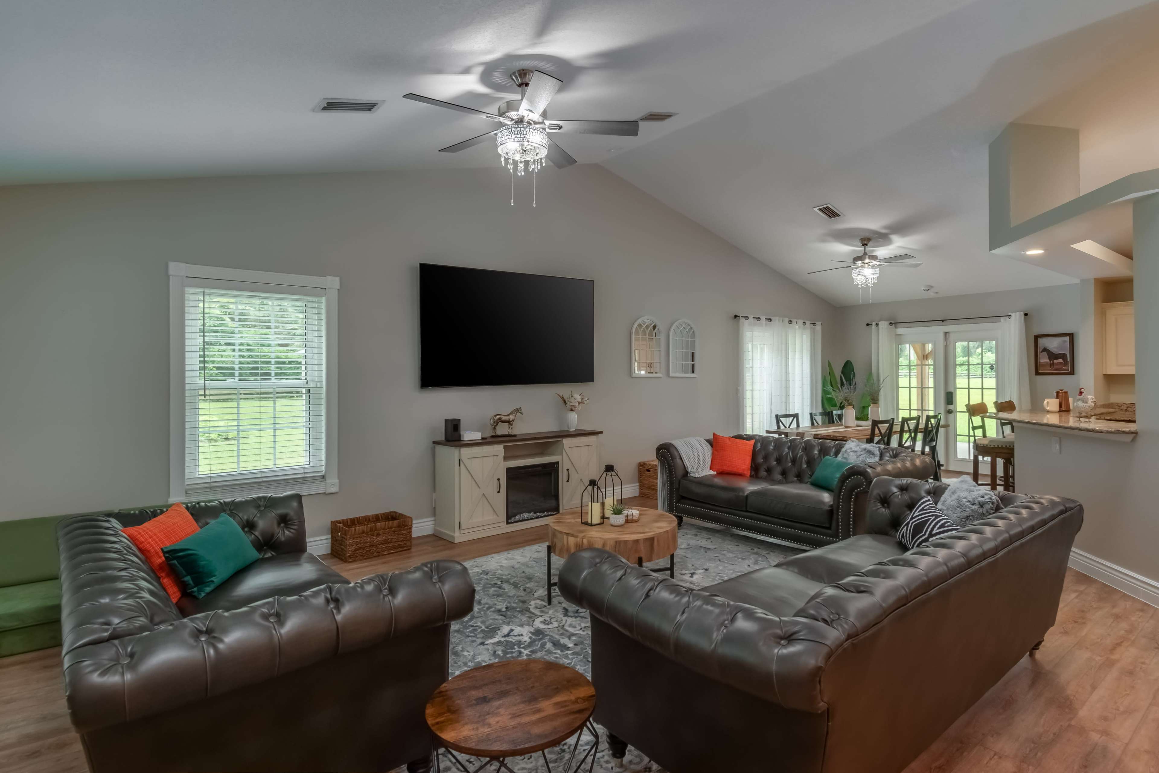 The living room features two dark leather sofas facing a wall-mounted television, with a dining area visible in the background.