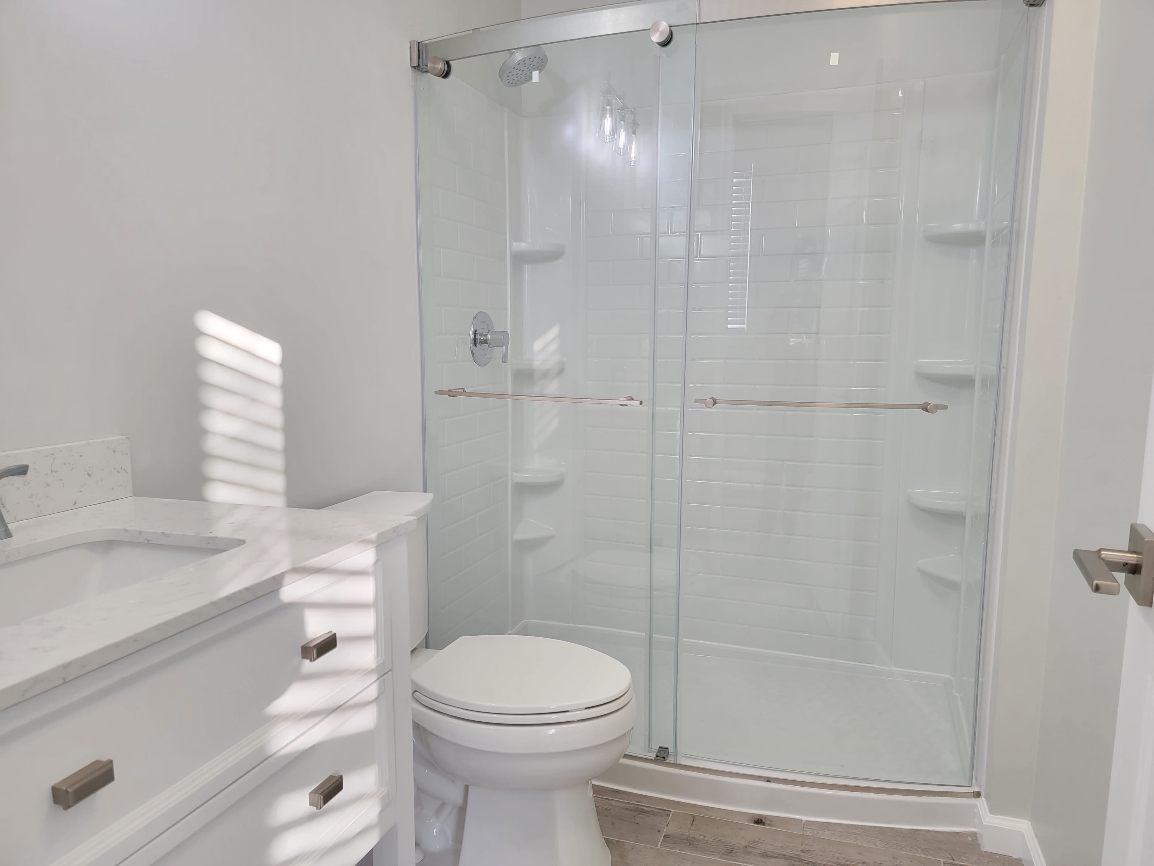 A modern bathroom featuring a glass-enclosed shower, a white vanity with a countertop, and a toilet.