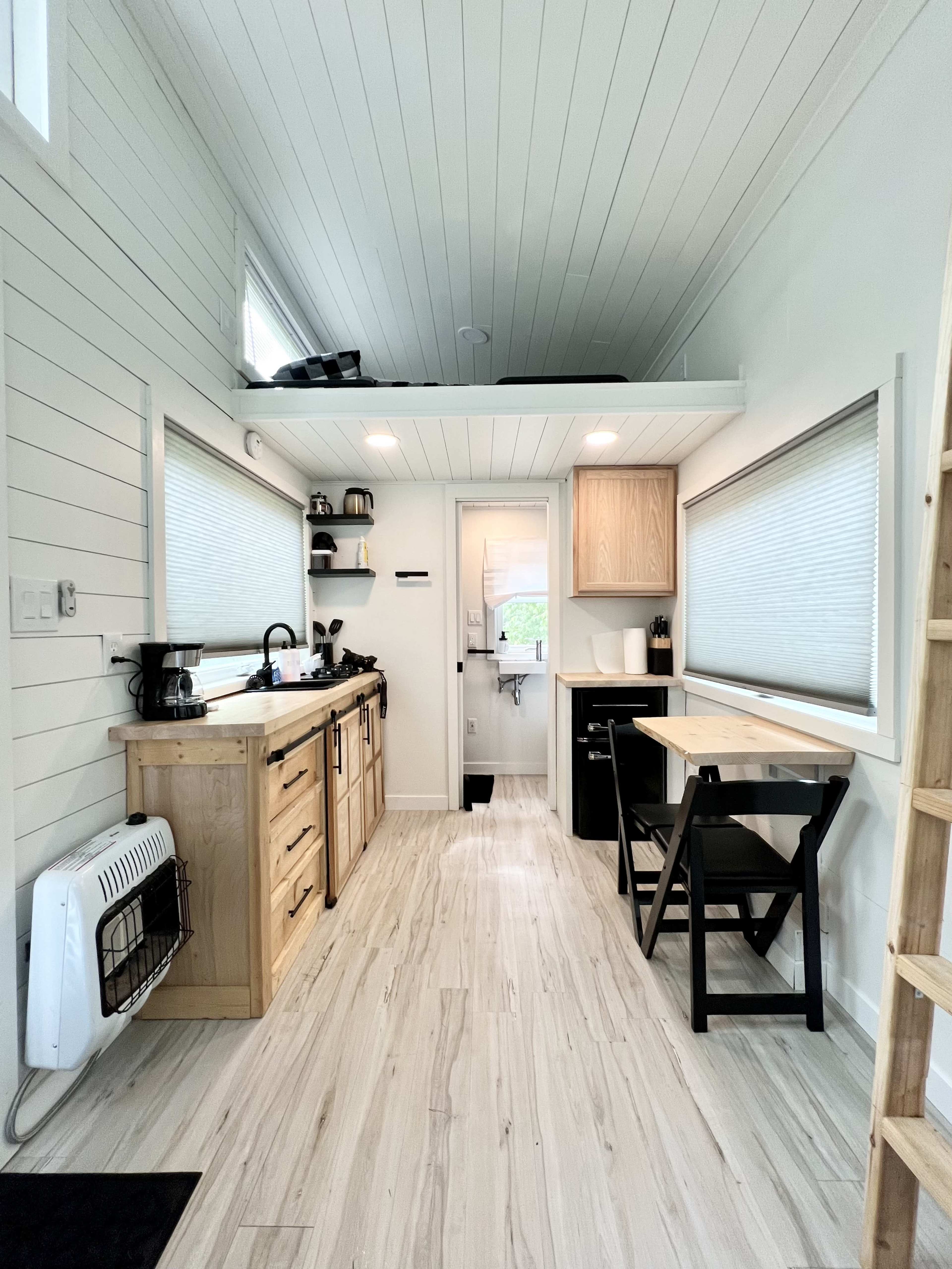 The interior of a compact kitchen and dining area in a small, modern home with a lofted sleeping space above.