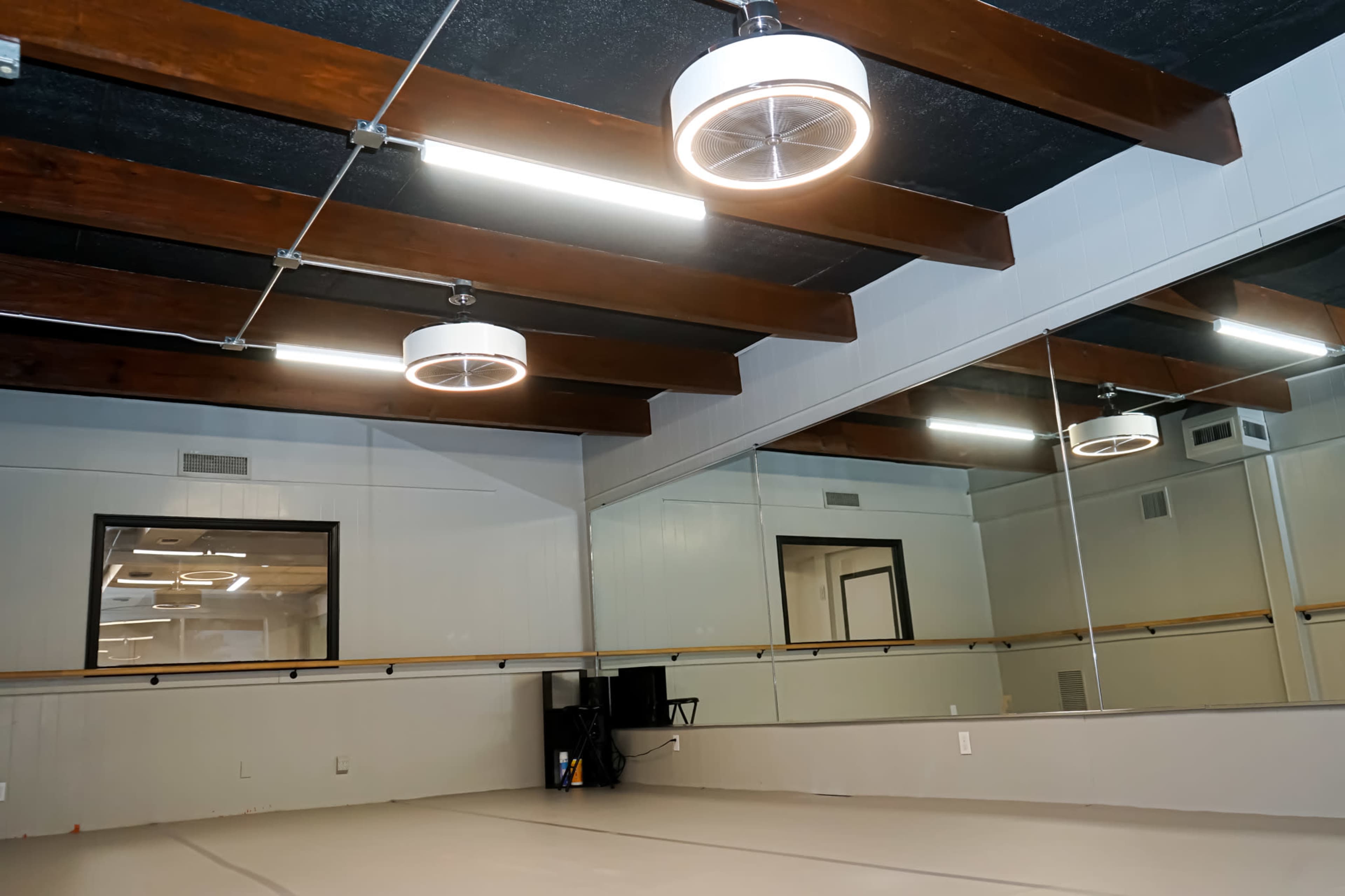 A dance studio featuring wooden beams, circular ceiling lights, and a large mirror along the wall.