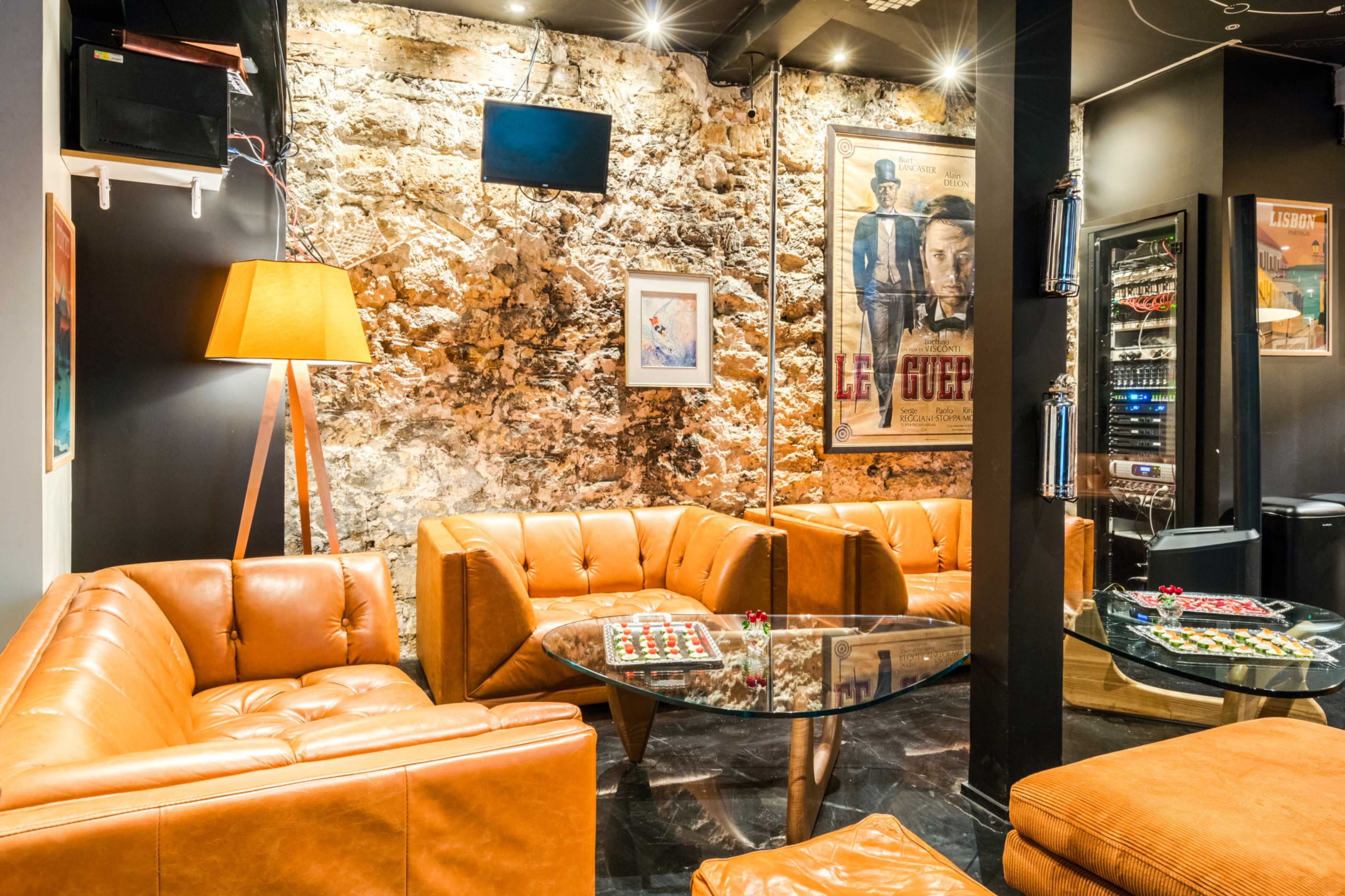 The image shows a cozy lounge area with leather sofas, a glass coffee table, and a wall featuring exposed stone and framed artwork.