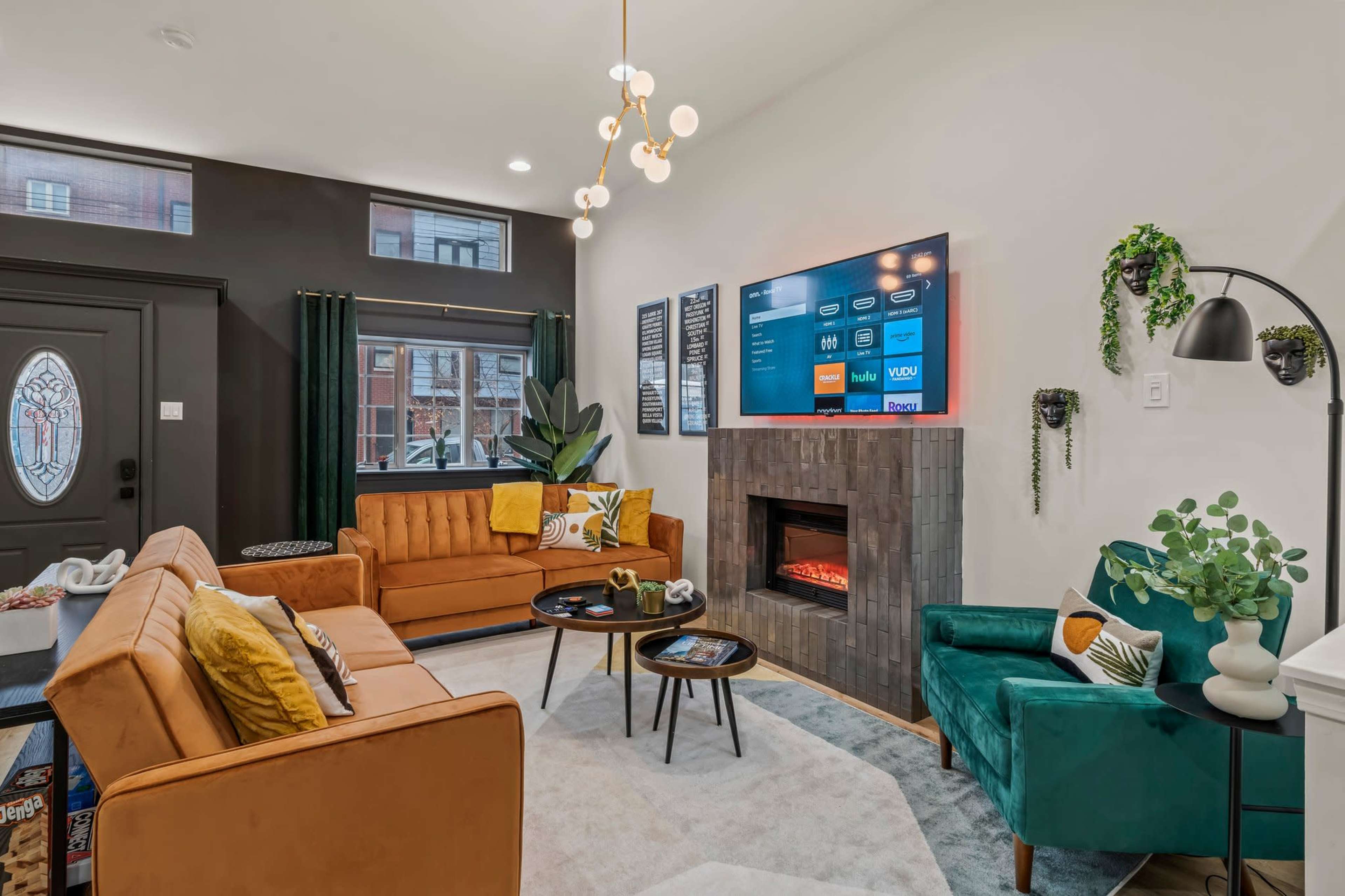 A modern living room features two sofas, a wall-mounted television, a fireplace, and decorative plants.