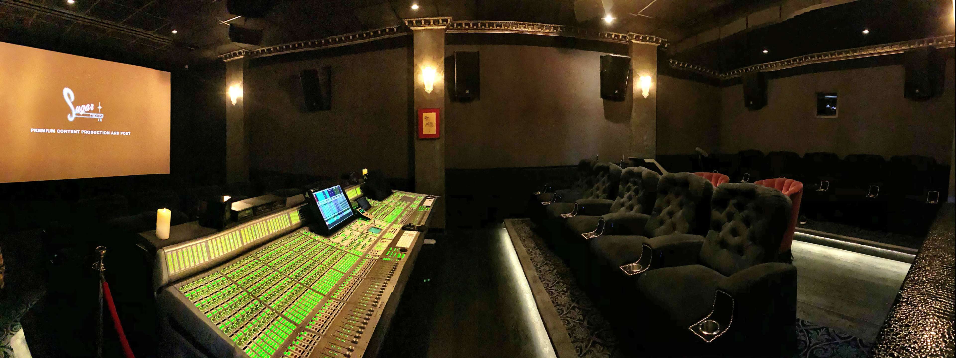 The image shows a dimly lit private screening room featuring a large sound mixing console and plush seating arranged in front of a projection screen.