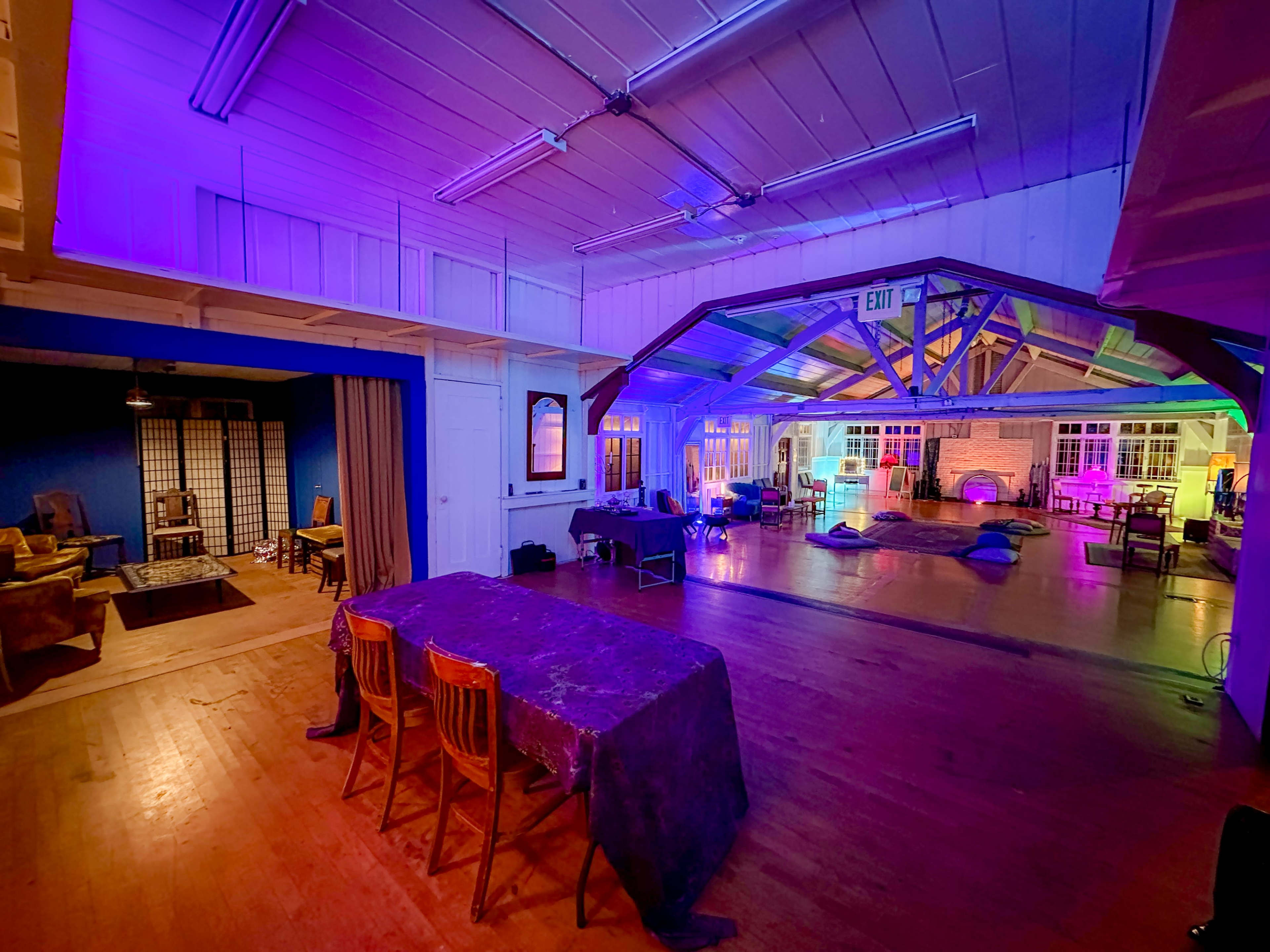 The image depicts a spacious indoor area featuring a wooden floor, multiple seating arrangements, and colorful lighting that illuminates the walls and ceiling.