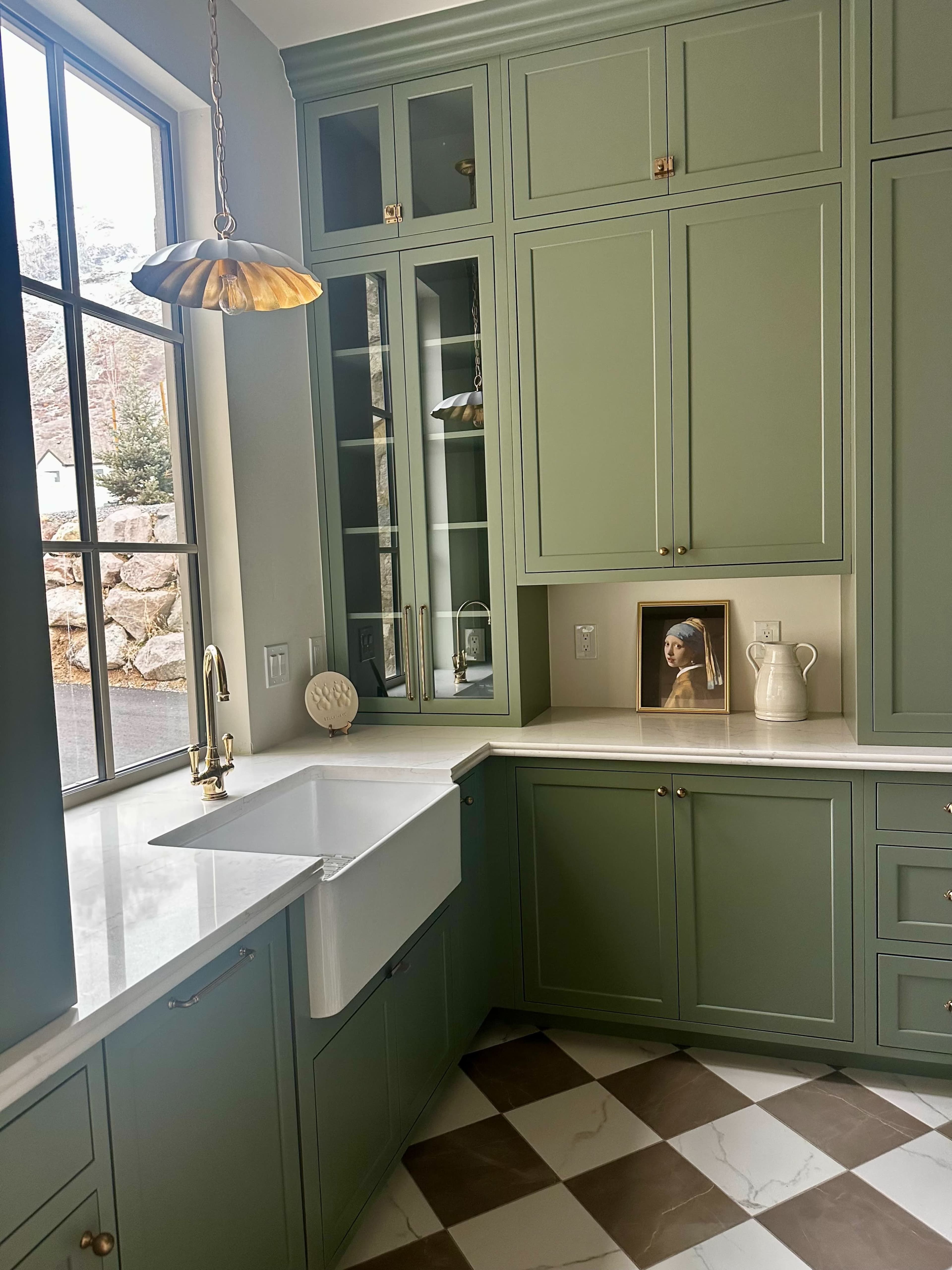 The image shows a modern kitchen featuring green cabinetry, a large farmhouse sink, and a checkered floor pattern.