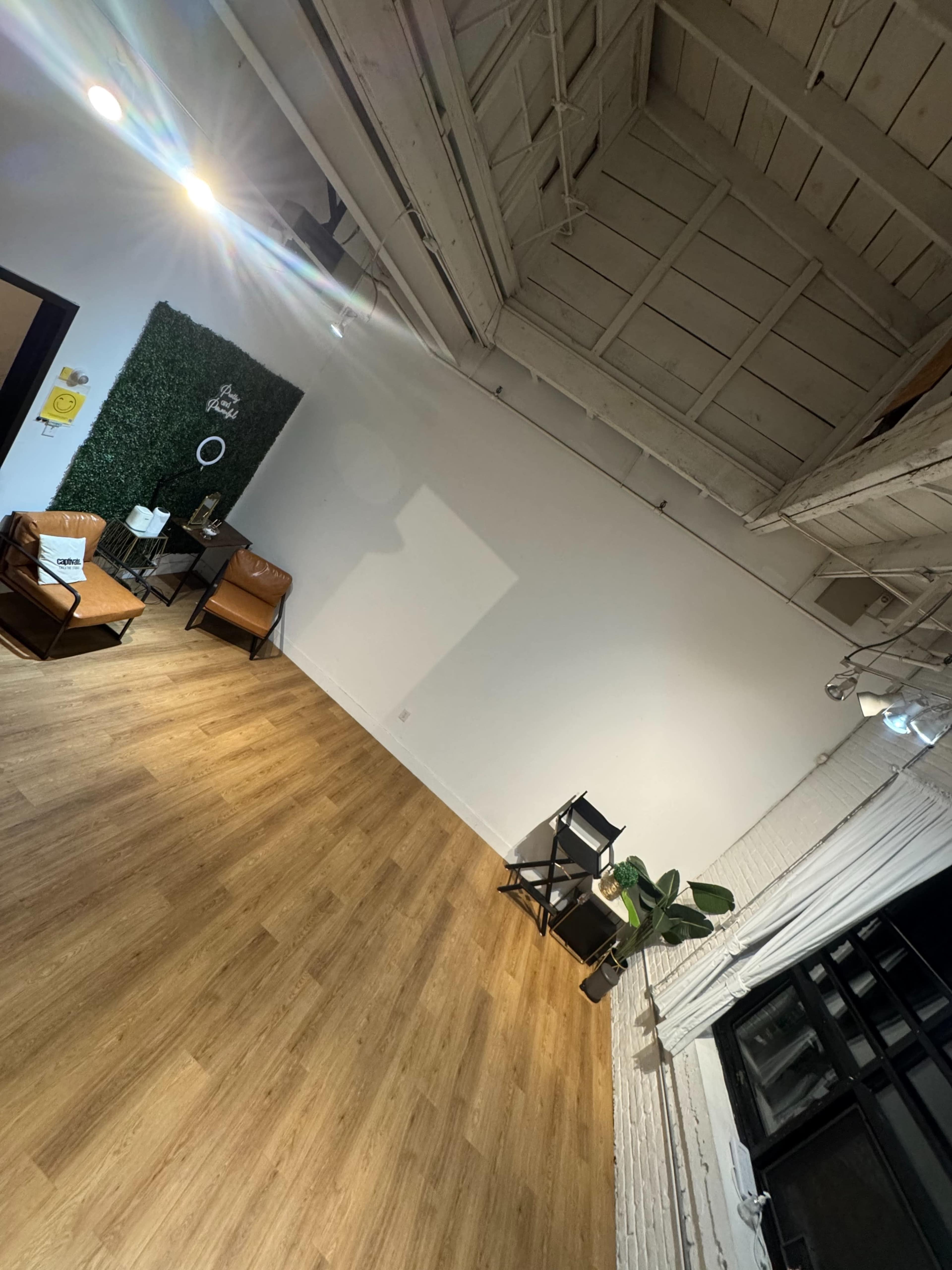 The image depicts a spacious, minimalist interior with wooden flooring, a green wall feature, and furniture arranged on one side.