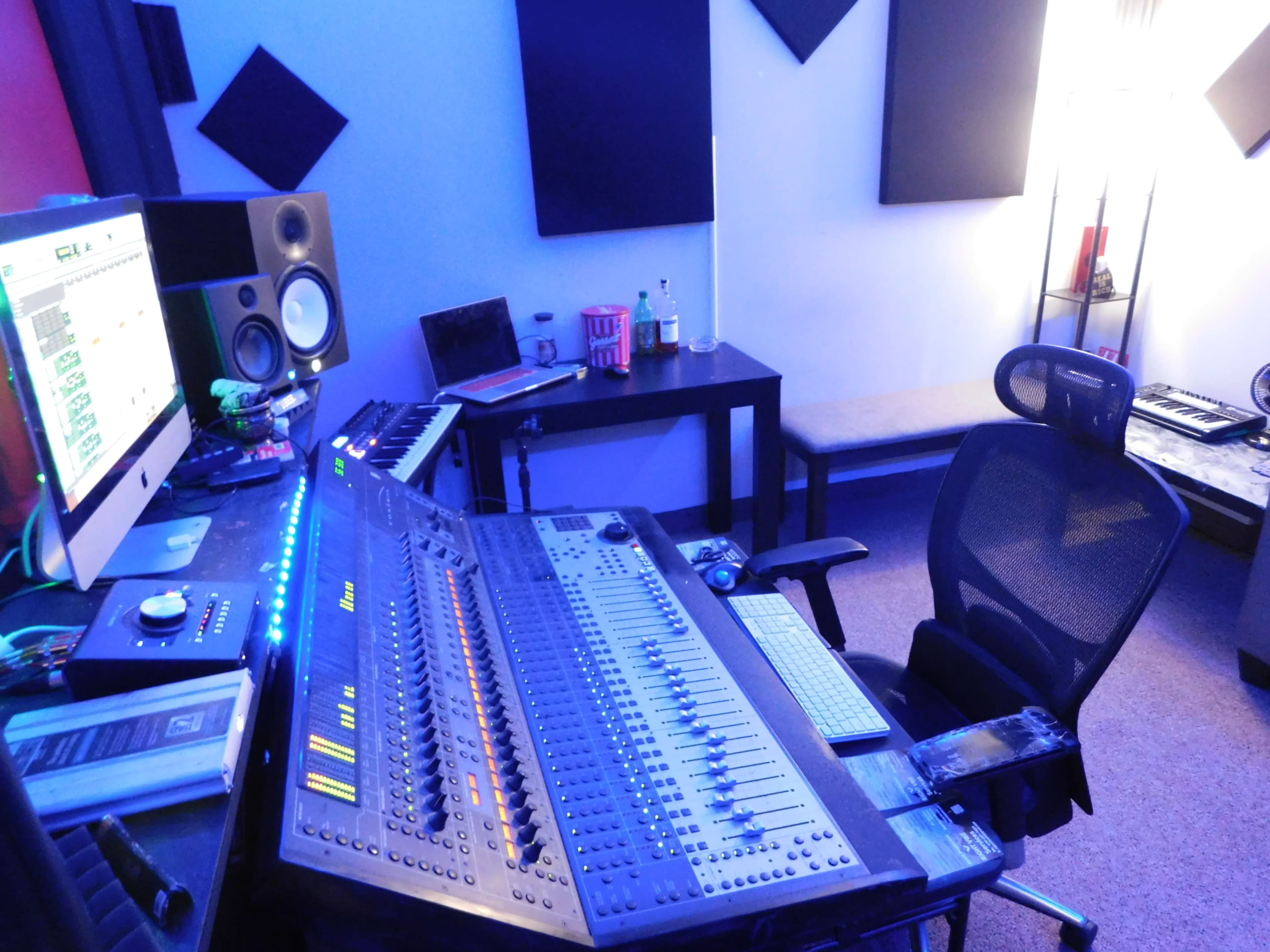 A music studio featuring a mixing console, computer monitor, keyboard, and various audio equipment arranged in a well-organized setup.