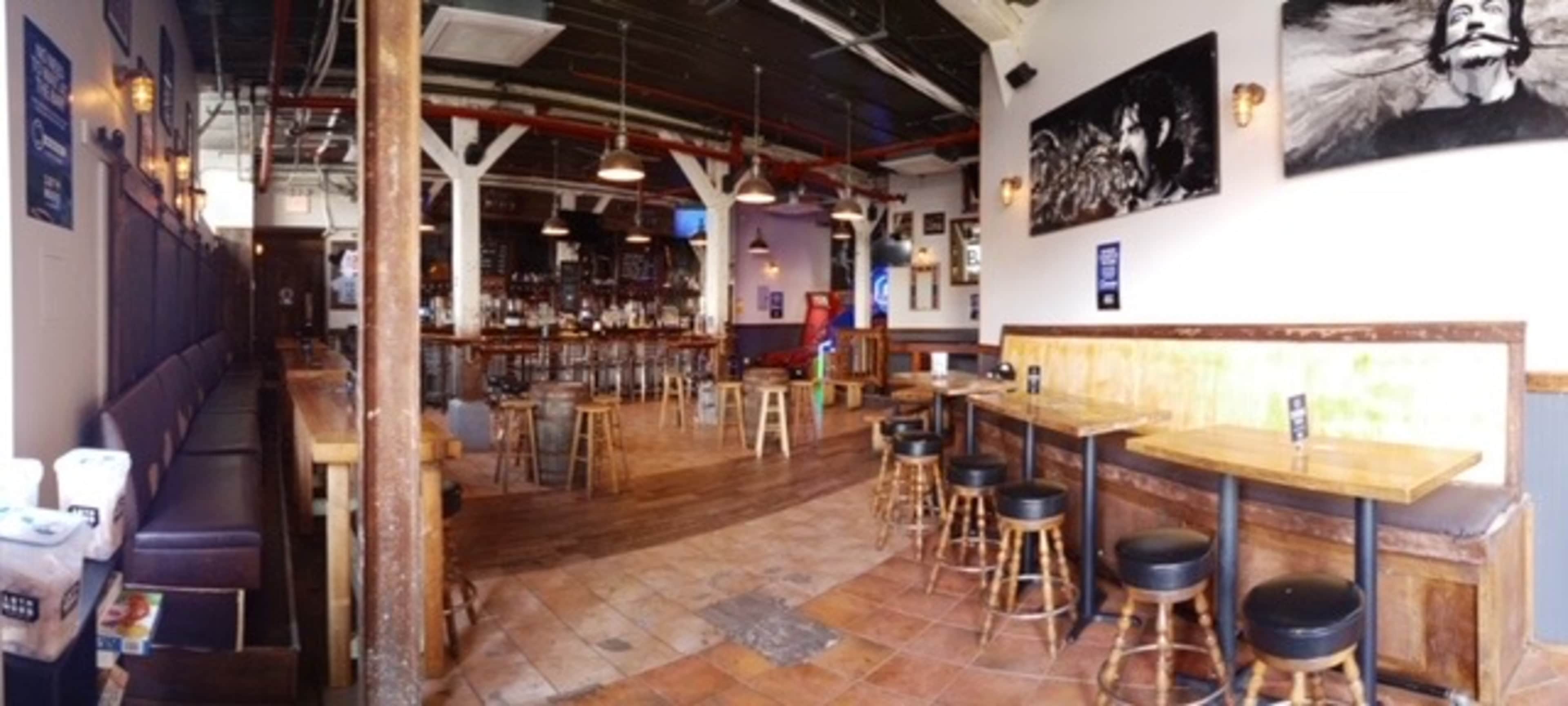 A spacious bar with wooden tables and stools, a long counter, and artwork on the walls.