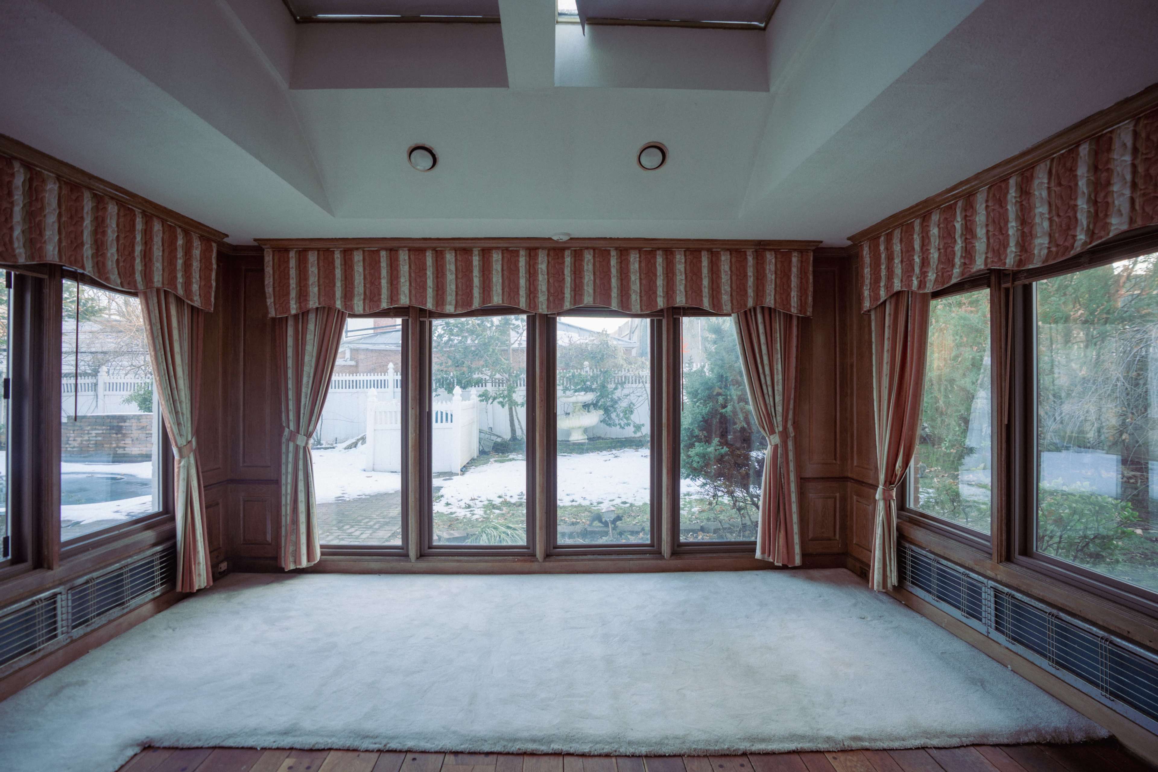 The image shows a vacant room with large windows covered by striped curtains, overlooking a snow-covered landscape.