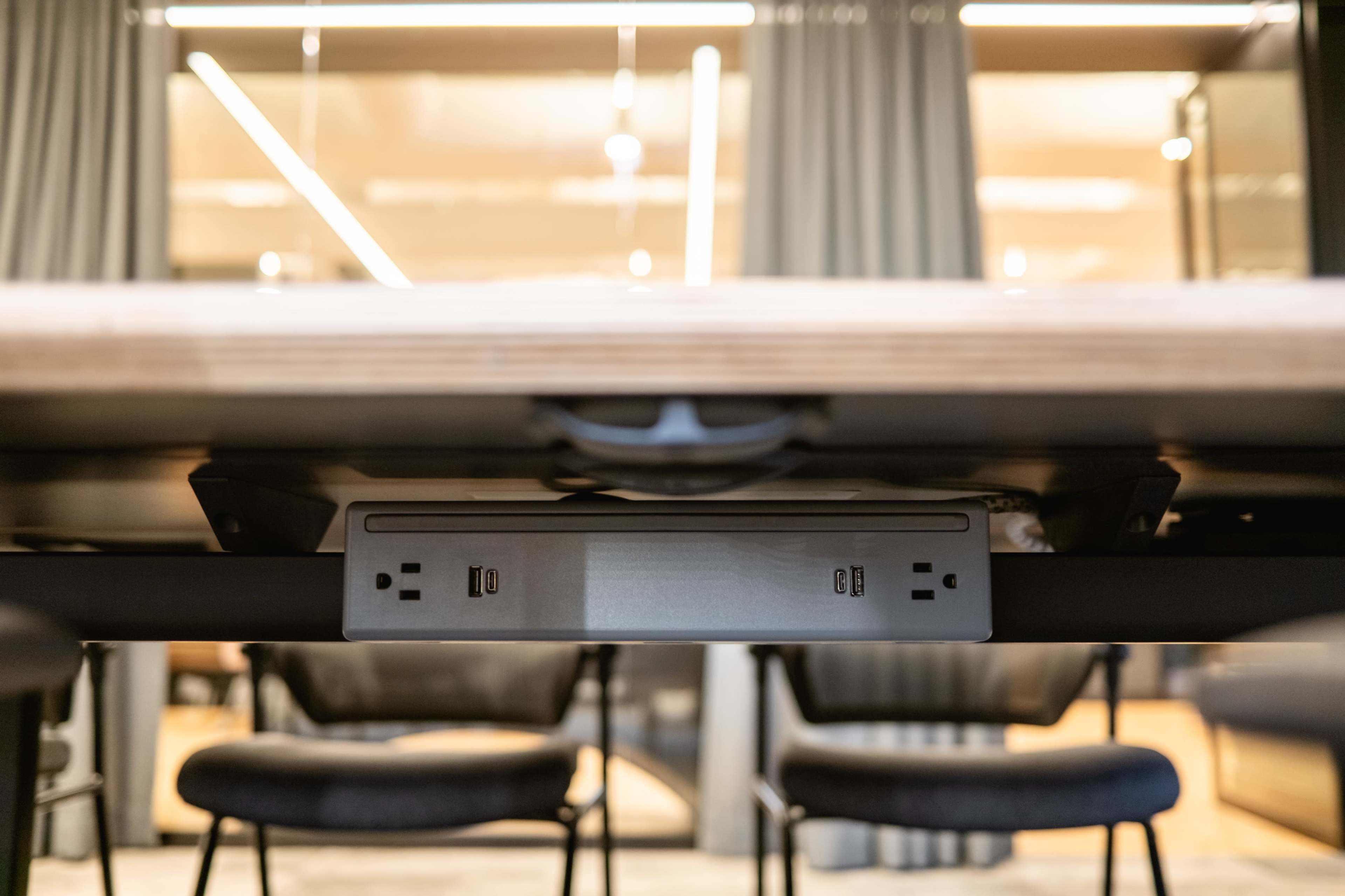The image shows the underside of a conference table with a power outlet and USB ports mounted on the surface.