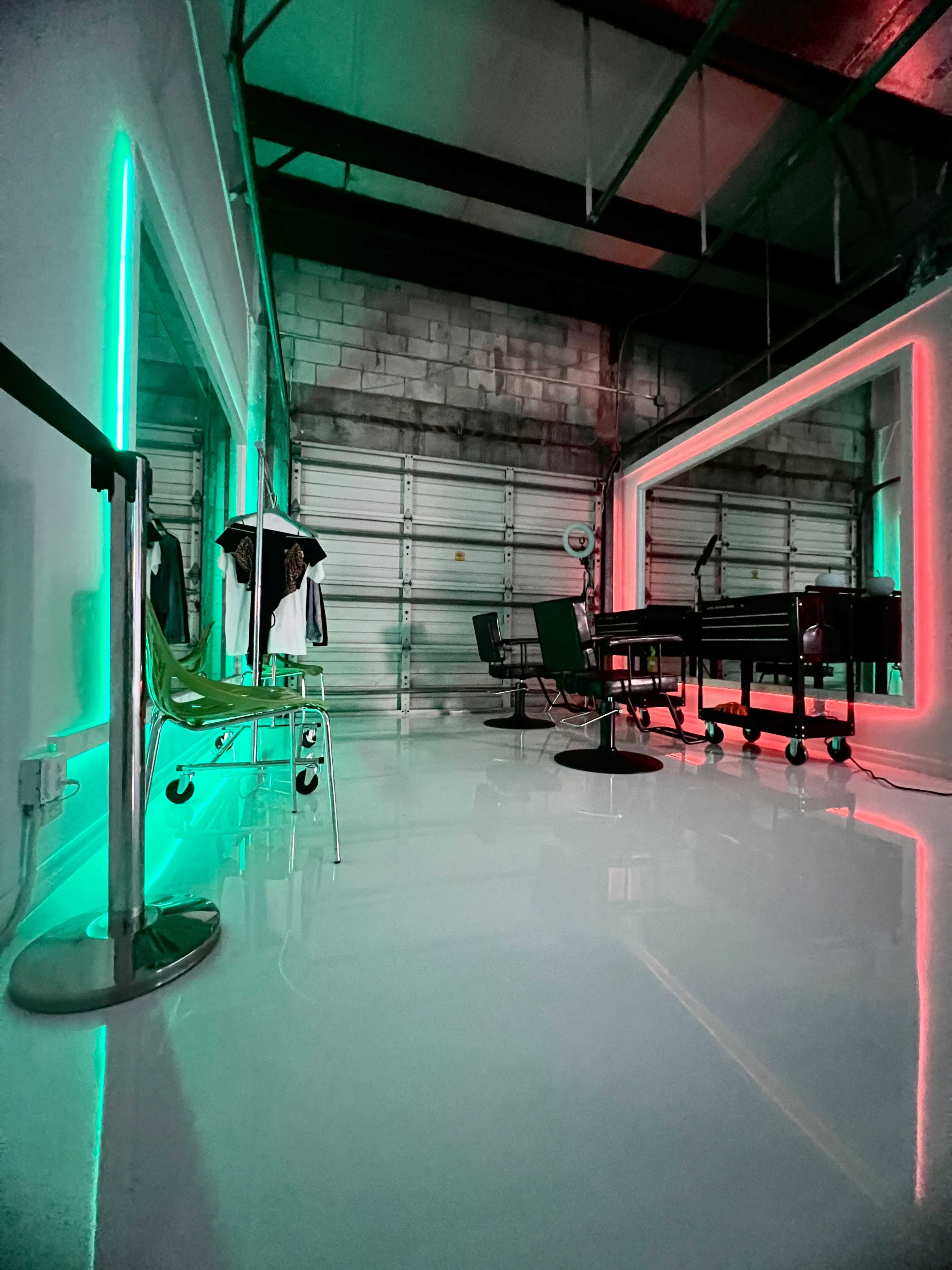 A modern studio space featuring colorful neon lights, a clothing rack, and a large desk in a warehouse setting.