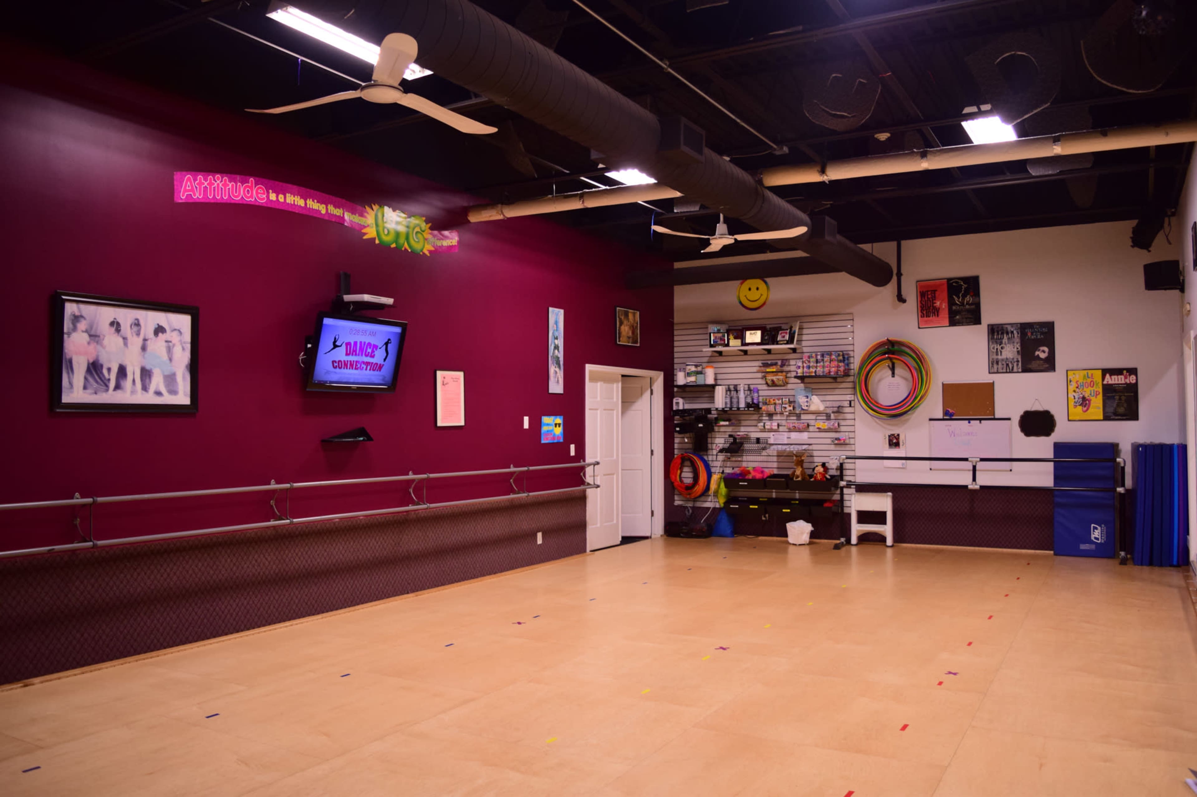 An indoor dance studio with a maroon wall, mirror, barres, and various dance props neatly organized on shelves.