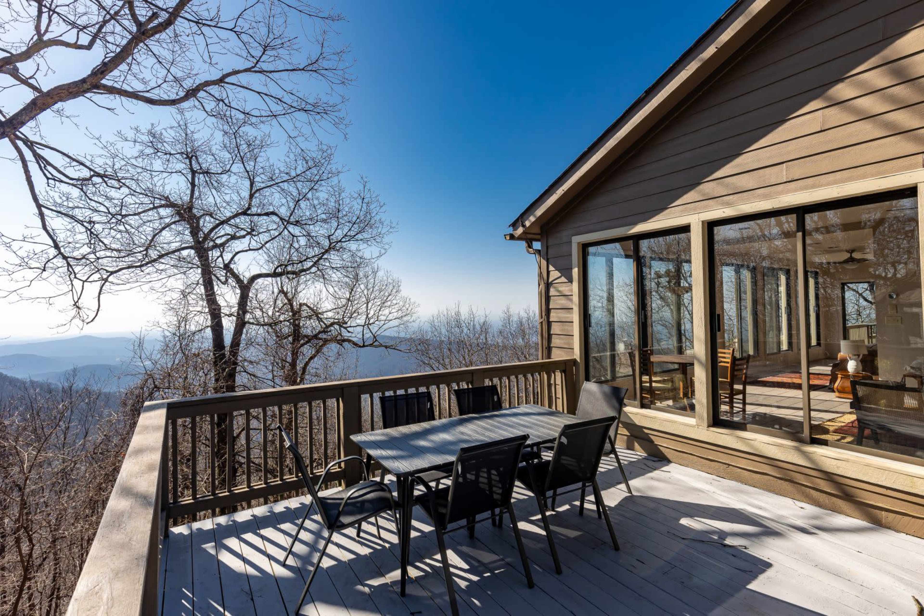 A patio with a dining table and chairs overlooks a mountainous landscape under a clear blue sky.