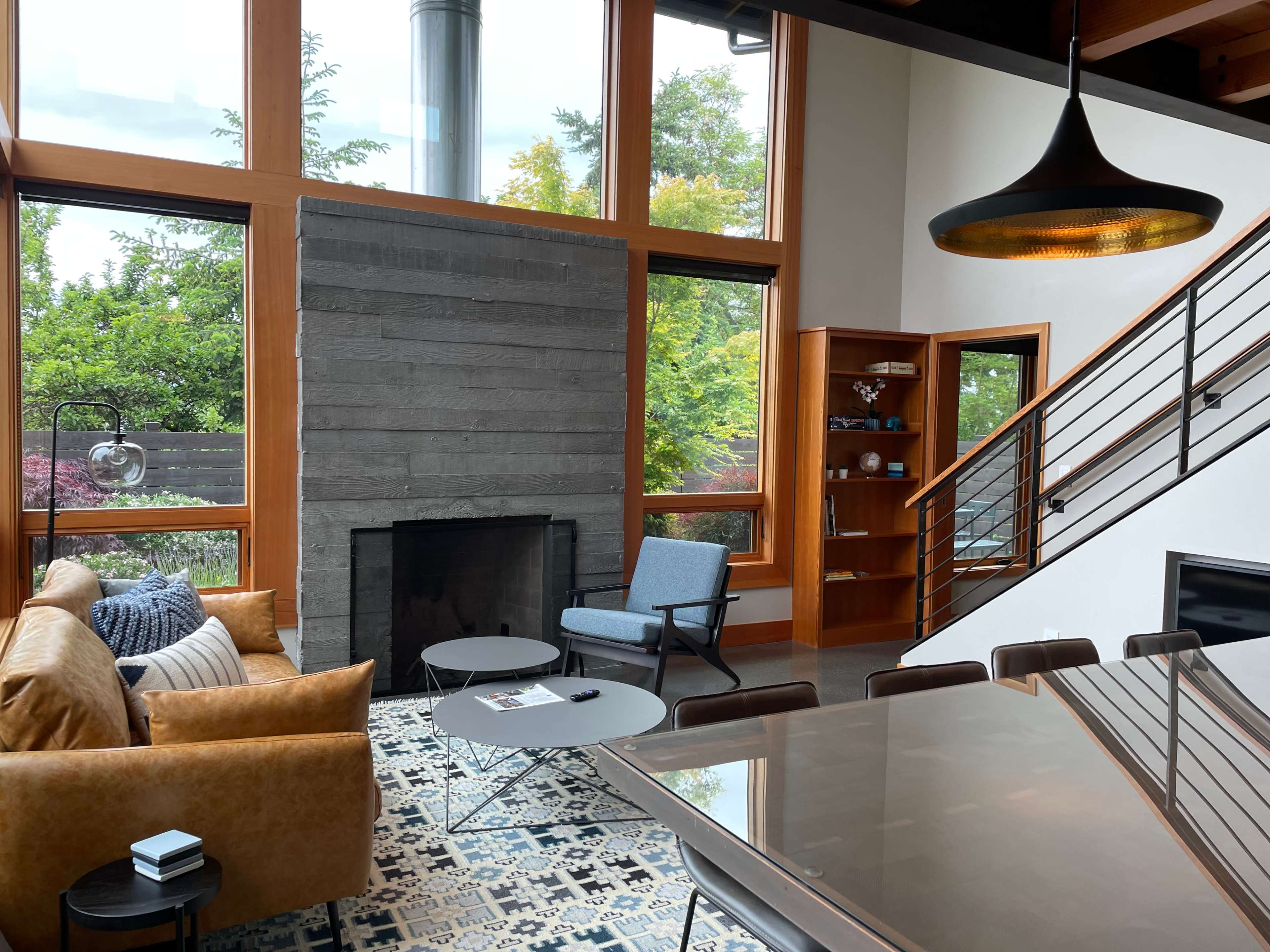 A modern living room features large windows, a stone fireplace, a brown leather sofa, and a dining area with a table.