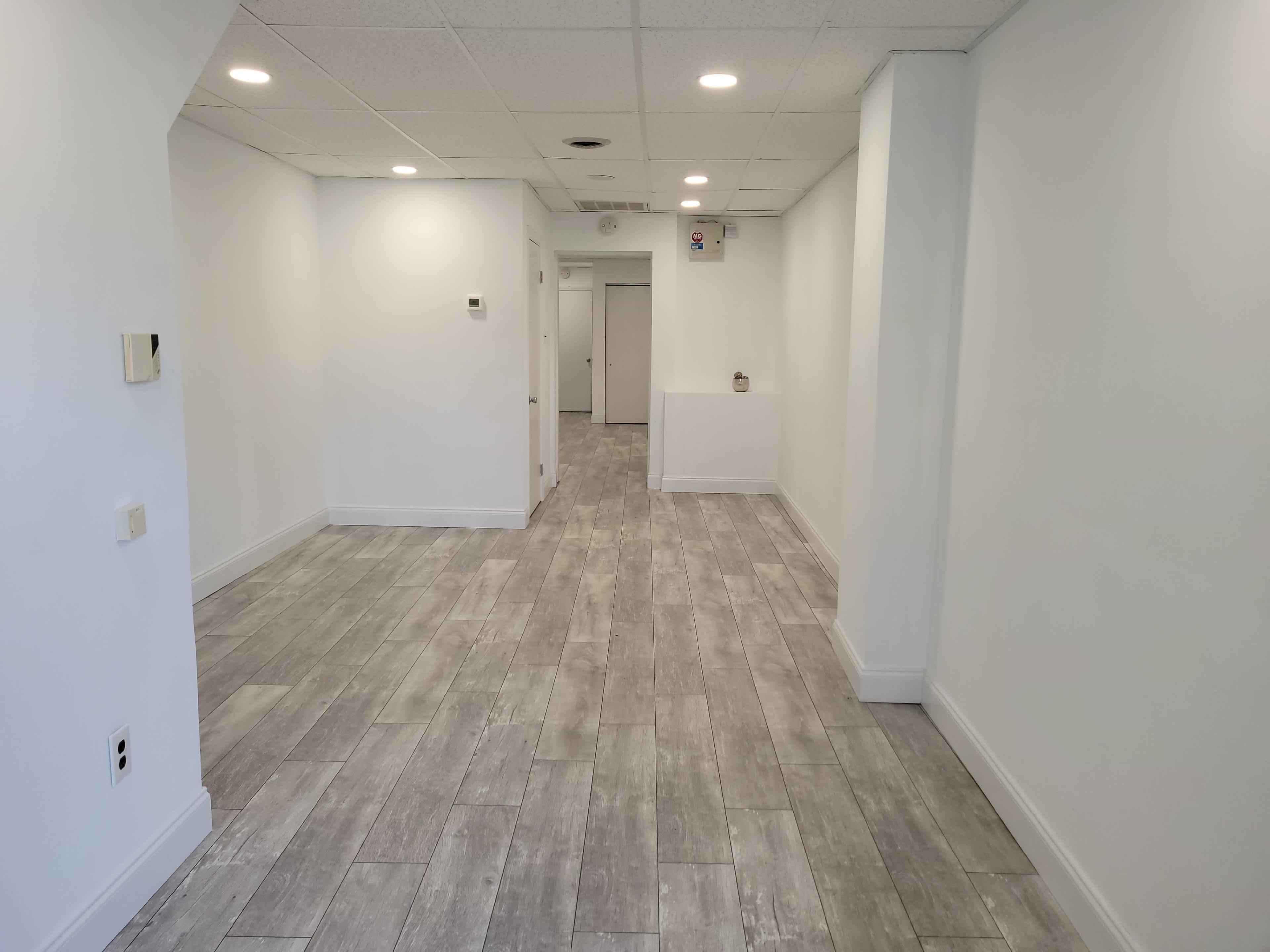 The image shows a spacious, empty indoor area with light-colored walls, tile flooring, and a few doorways visible in the background.