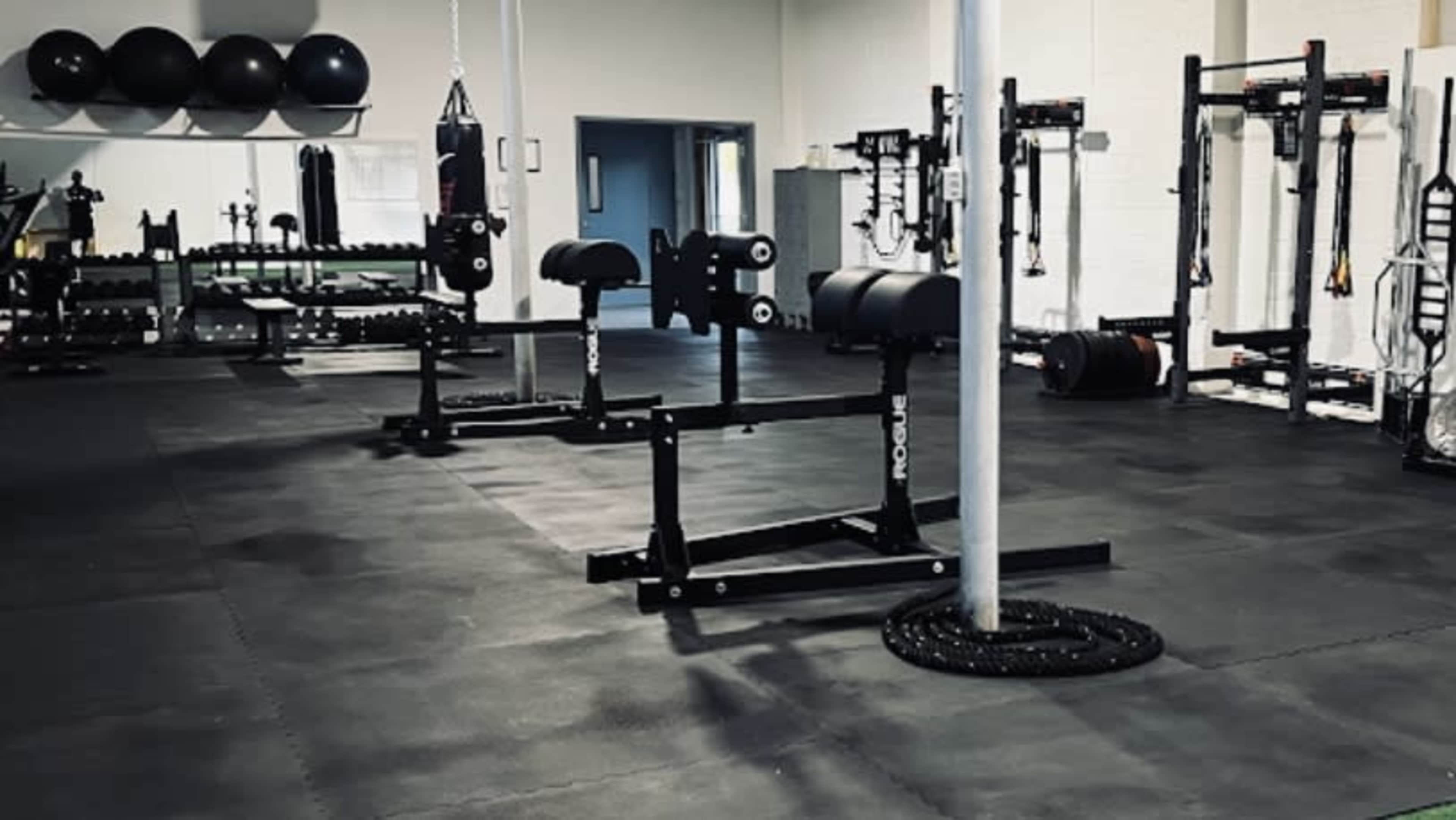 A gym interior with weightlifting equipment, including benches and racks, arranged on a rubberized floor.