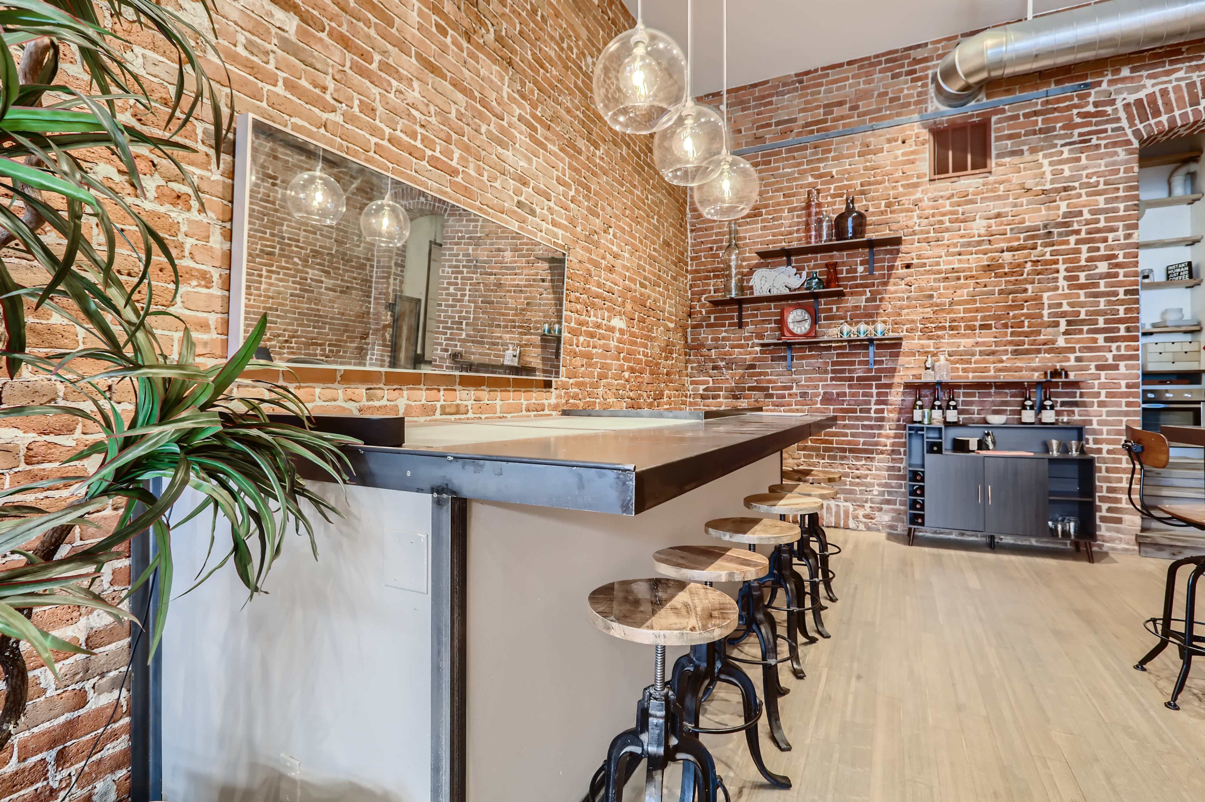 A bar area with a brick wall, a metal counter, and stools arranged along the front.