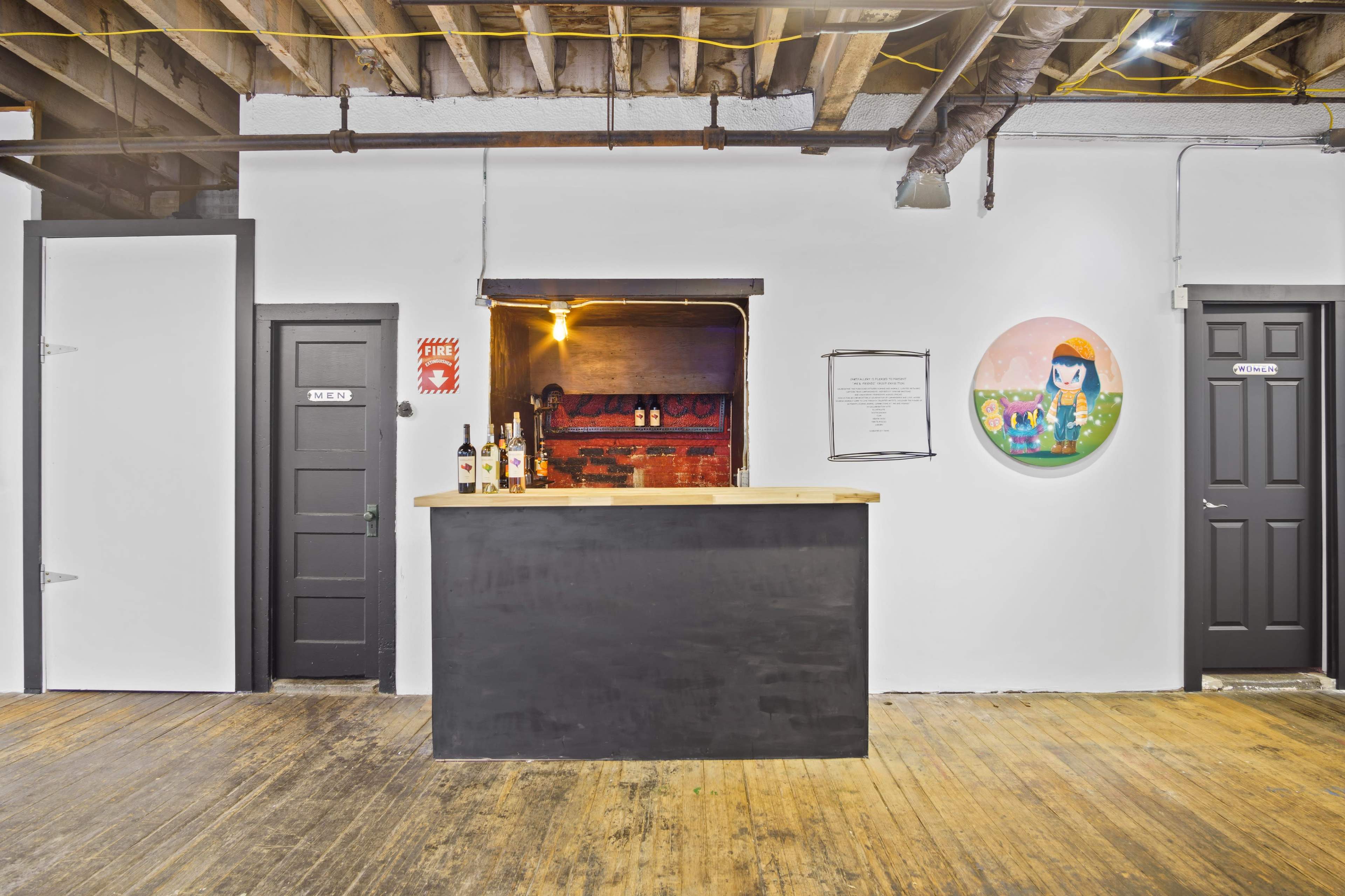 A minimalist bar area with a wooden counter, surrounded by dark doors and framed artwork on a white wall.