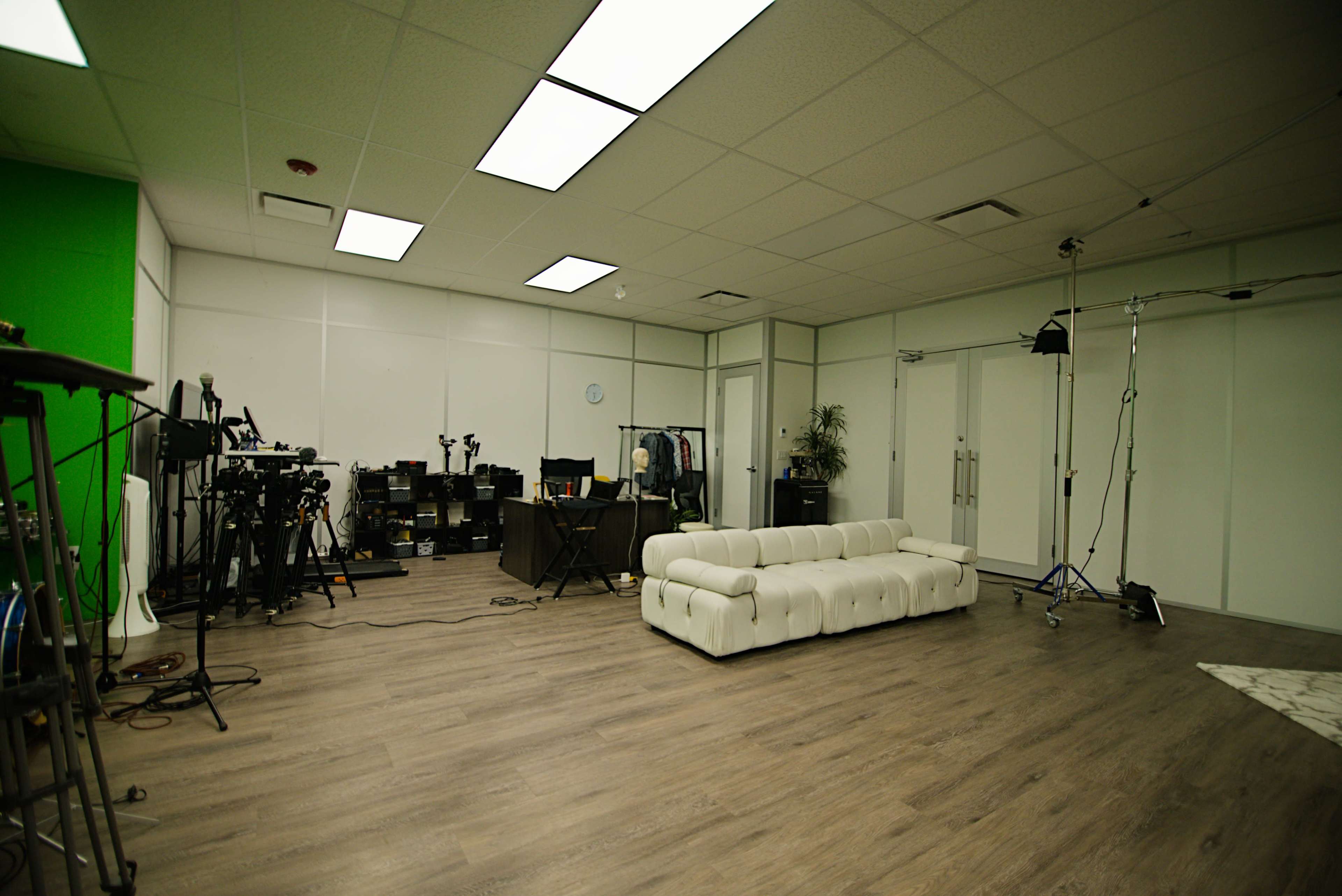 The image shows a spacious studio room with a white couch, various filming equipment, and a green backdrop.